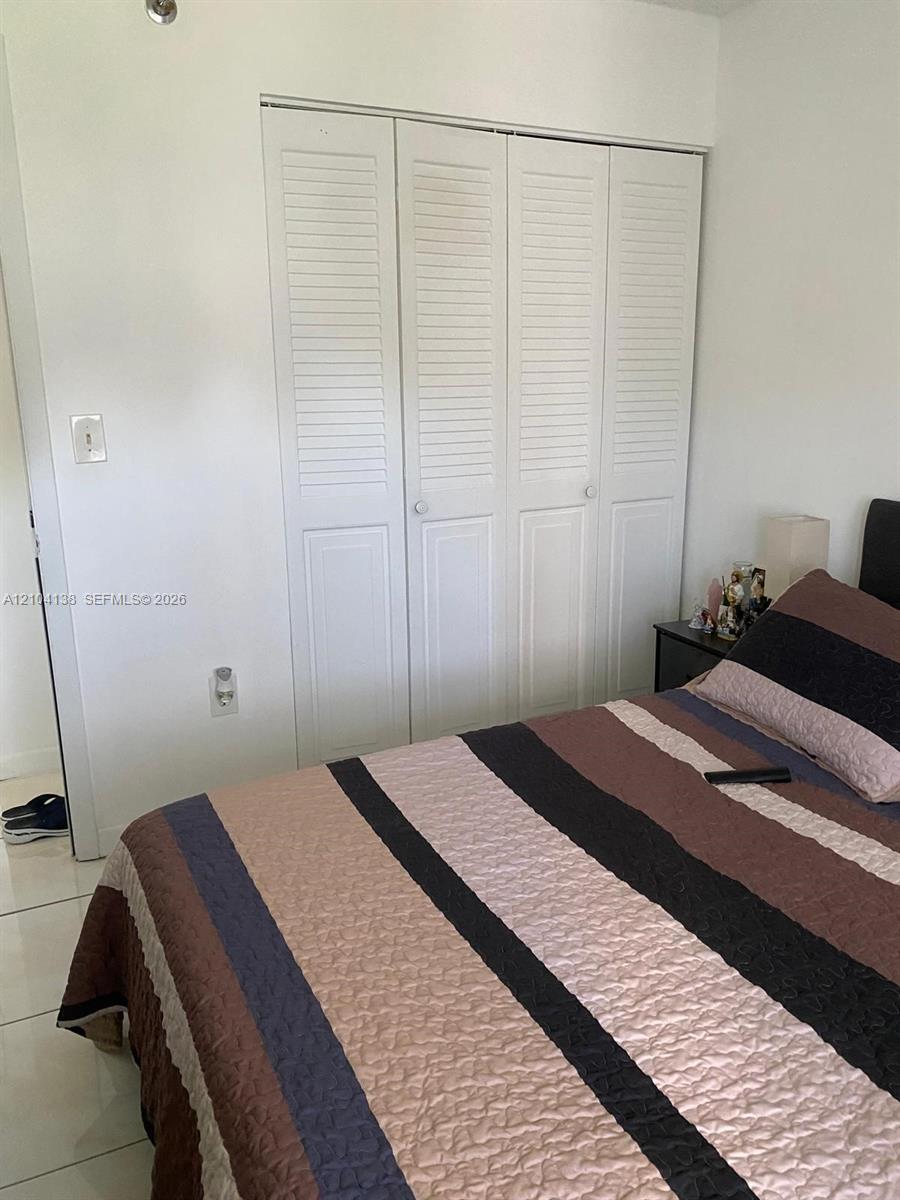 Four-panel closet featuring white louvered bifold doors and large-format tile flooring