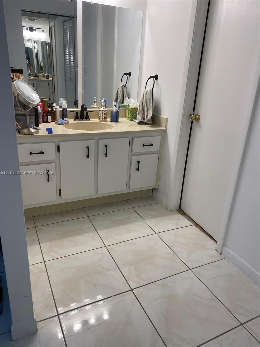 Bathroom vanity featuring white cabinetry, matte black hardware, a neutral countertop with an integrated basin, and a full-width wall mirror complemented by large-format ceramic floor tile