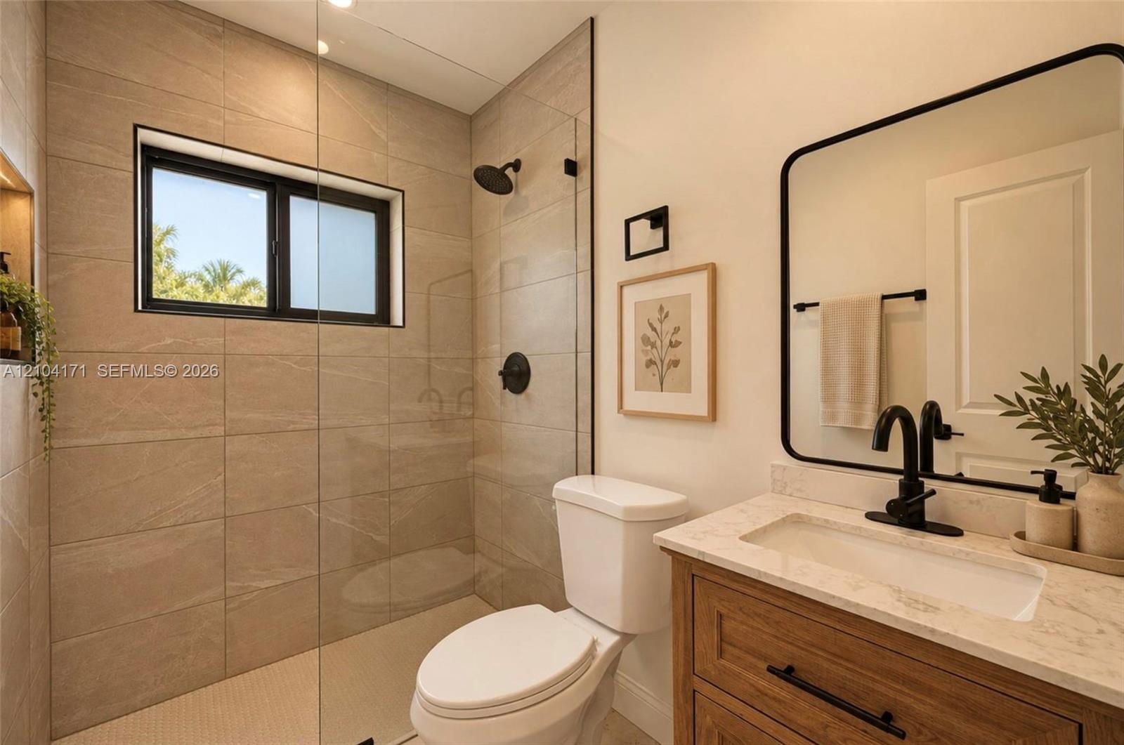 Bathroom featuring a glass-enclosed shower with floor-to-ceiling large-format tiling, wood-finish vanity with stone countertop, matte black fixtures, and a framed mirror