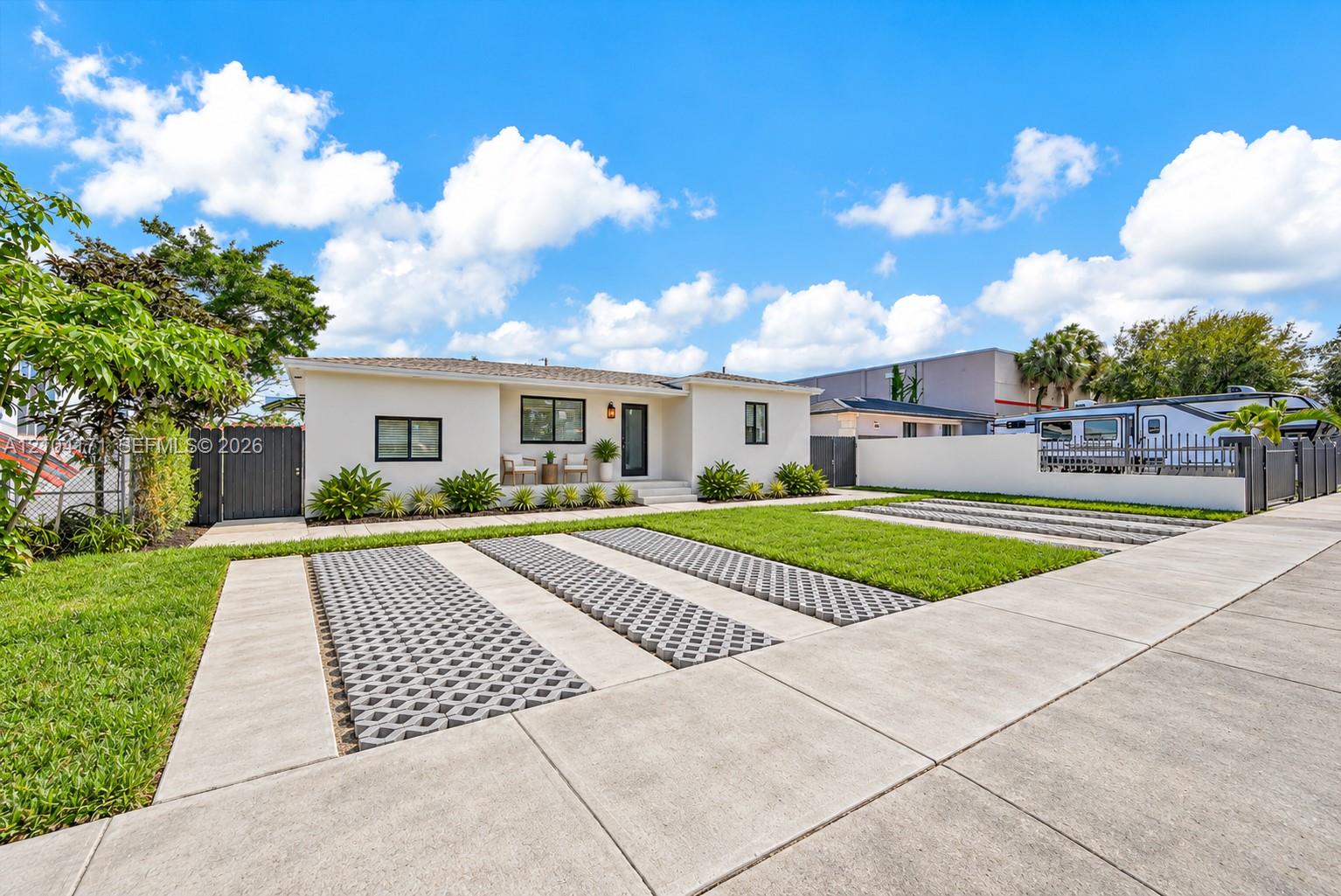 Single-story exterior featuring a light-toned stucco facade, multi-vehicle parking pad with decorative concrete pavers, and perimeter fencing