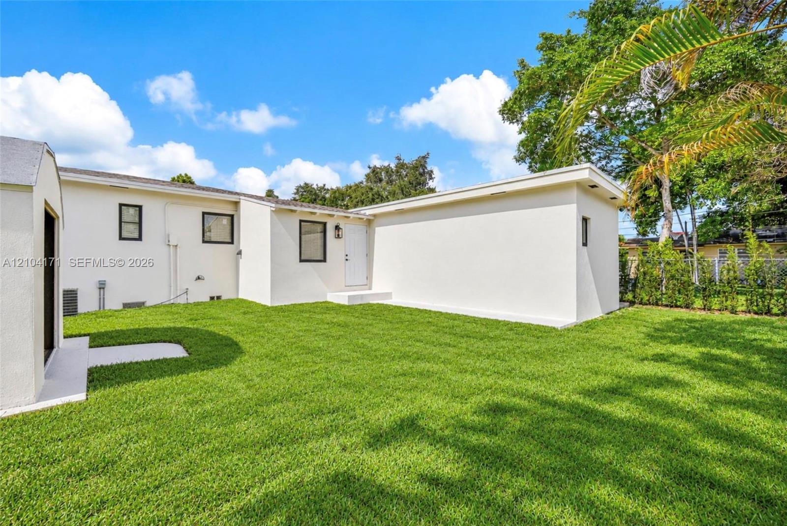 Backyard featuring a manicured lawn, smooth stucco exterior, and mature perimeter trees