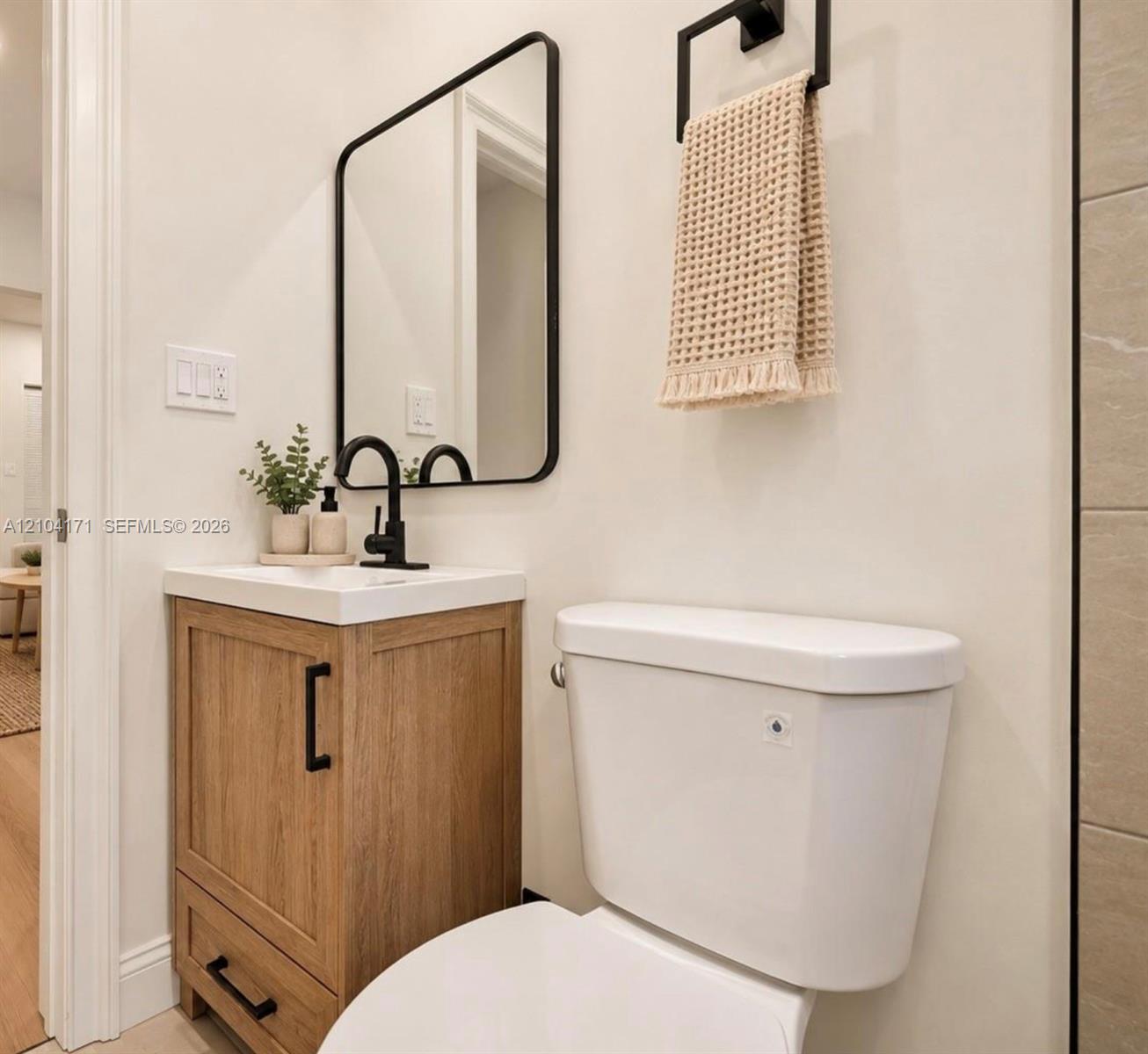 Wood-finish vanity with a rectangular sink, matte black faucet, rounded rectangular mirror, and matte black towel hardware