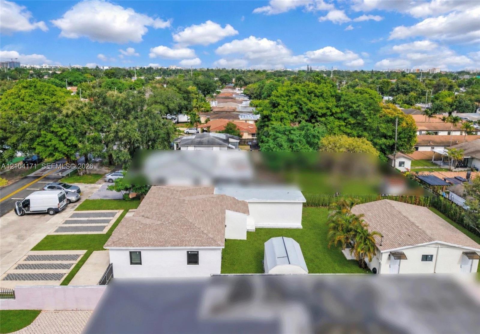 Aerial perspective featuring a detached structure, paved multi-vehicle parking area, and expansive lawn space
