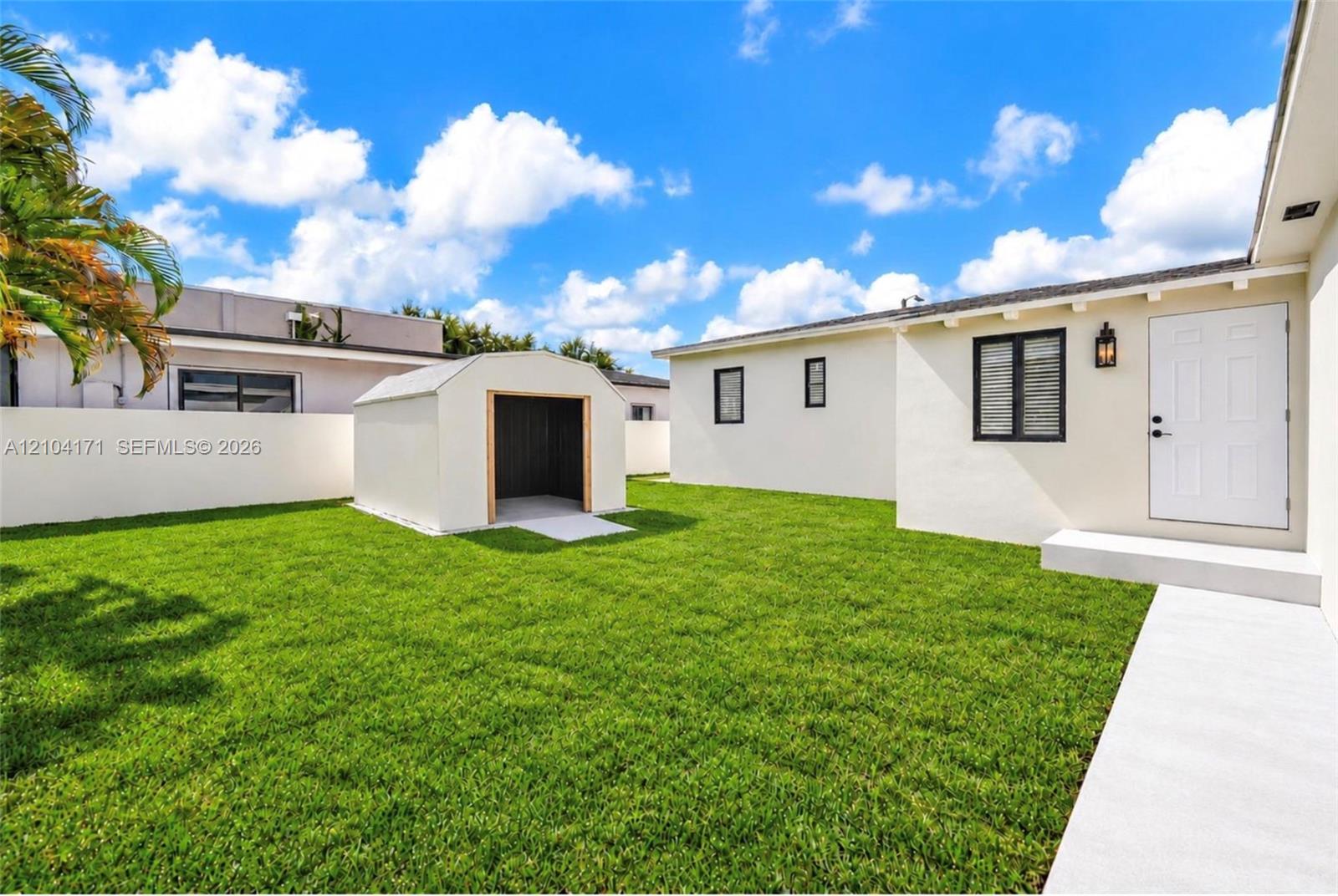 Backyard featuring a manicured lawn, perimeter masonry wall, detached storage shed, and concrete walkway