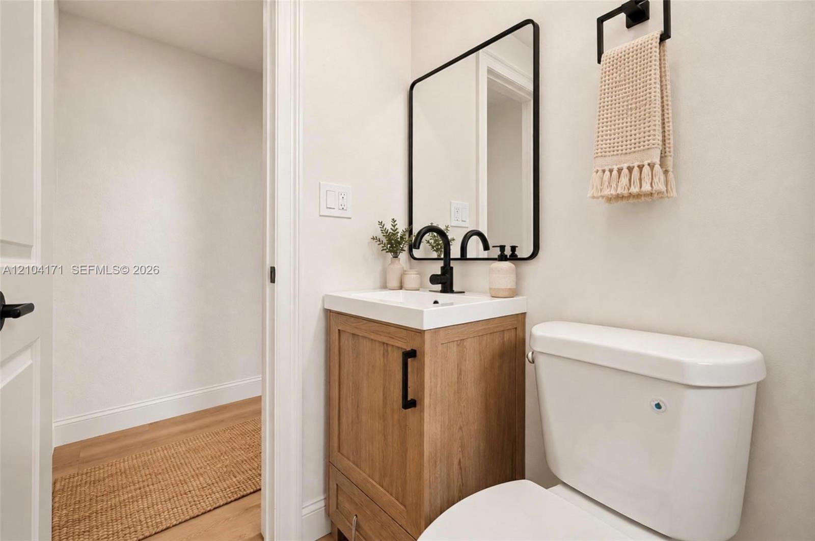 Wood-finish vanity with a rectangular sink, matte black faucet, wall-mounted rectangular mirror with a black frame, and a coordinating matte black towel ring
