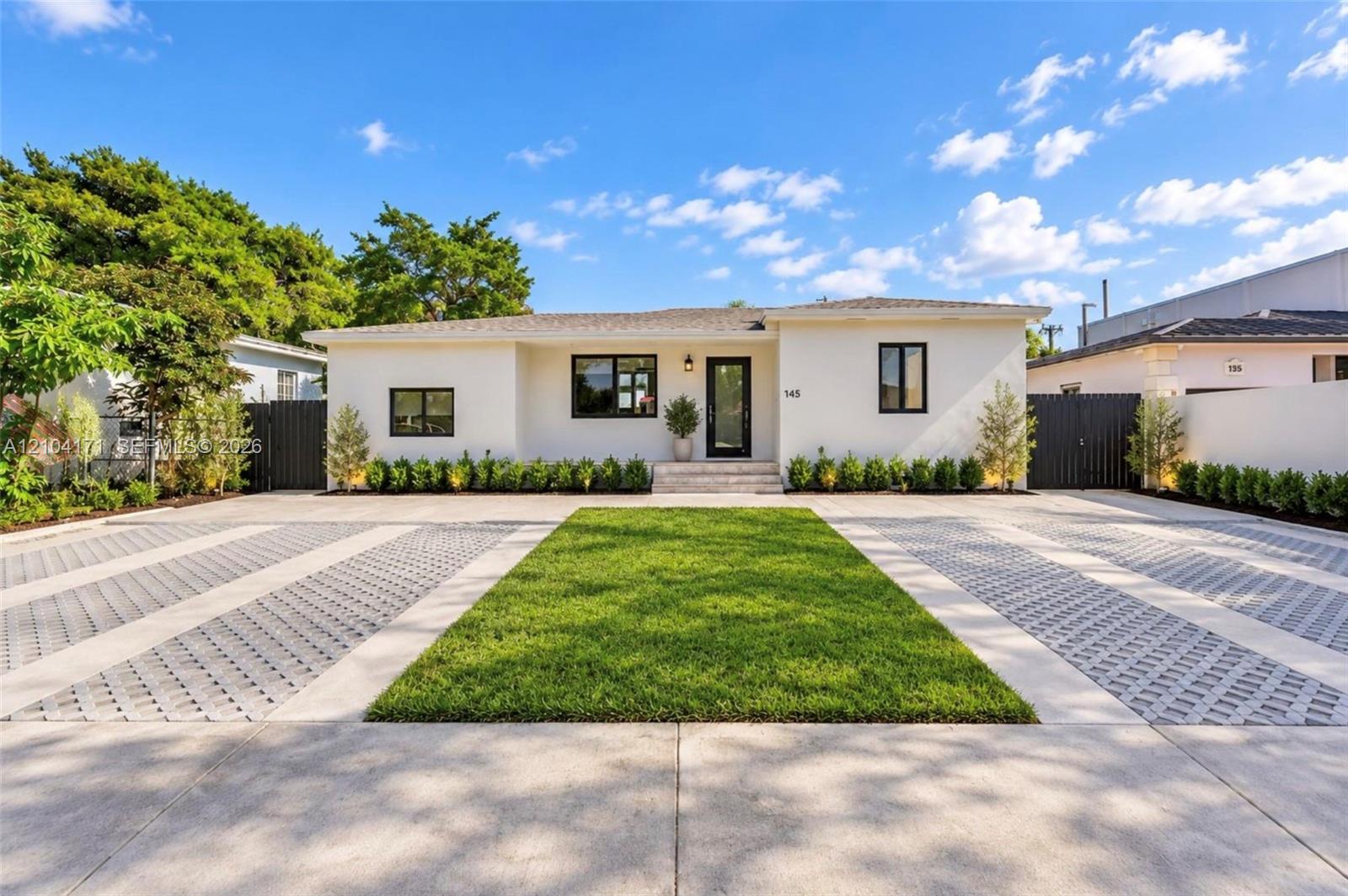 Single-story residence featuring a smooth stucco facade, contrast-trimmed windows, a central entryway with stone steps, and an expansive paved motor court with integrated turf landscaping