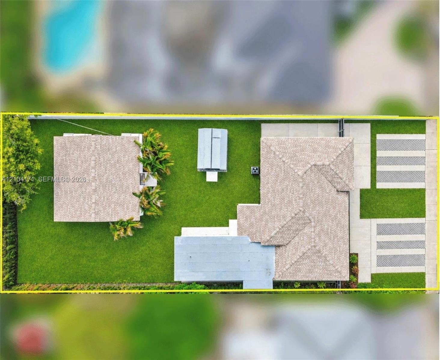 Aerial view of property featuring a detached structure, manicured lawn, paved driveway, and perimeter fencing
