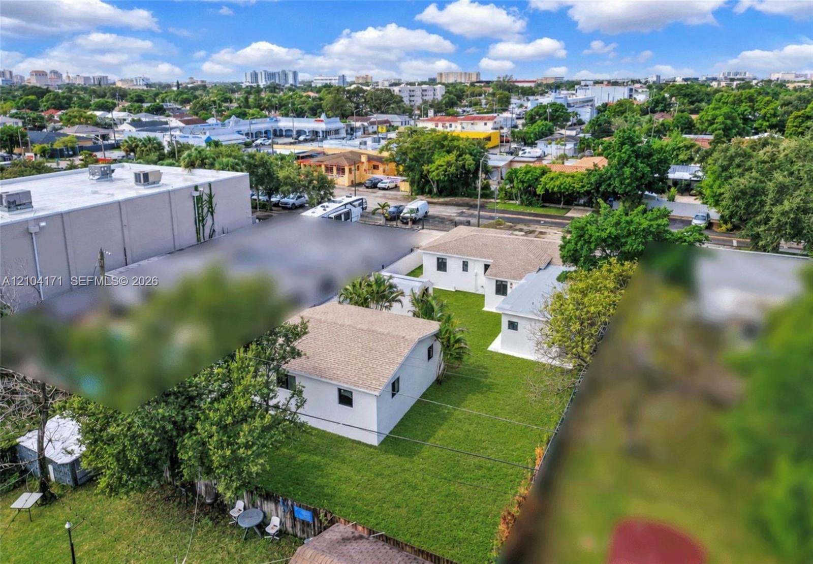 Aerial perspective of property featuring multiple structures, expansive green space, mature landscaping, and perimeter fencing
