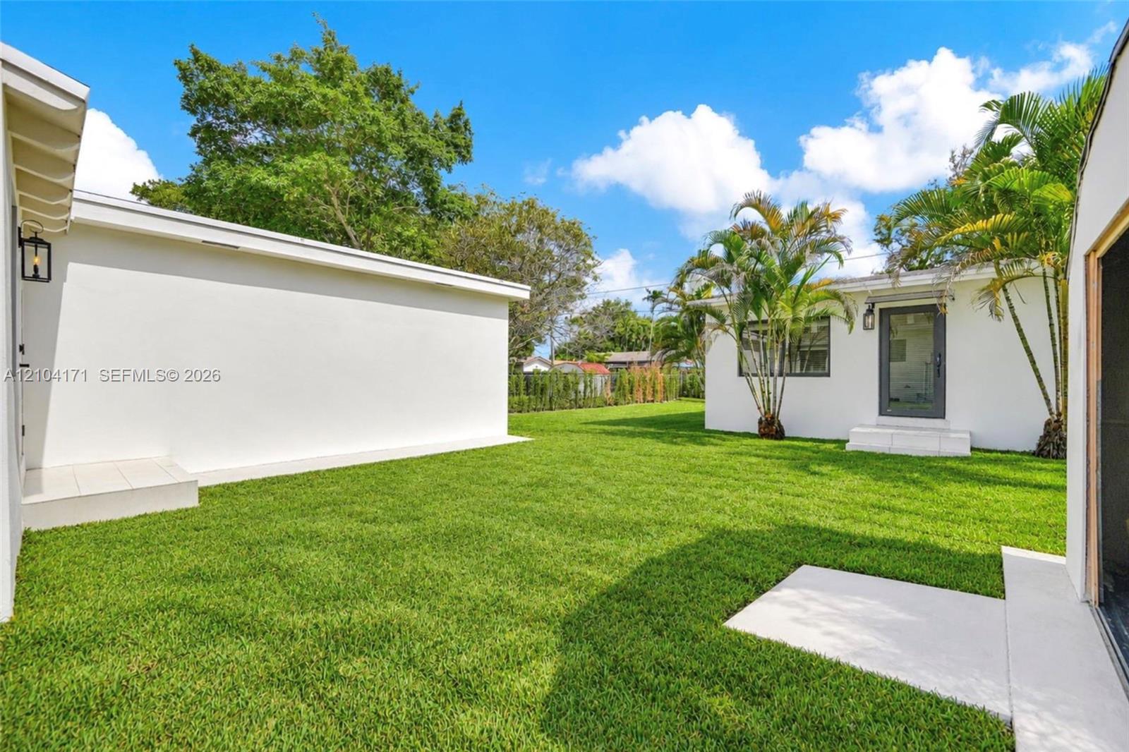 Expansive backyard featuring a manicured lawn, concrete patio surfaces, and mature palm trees