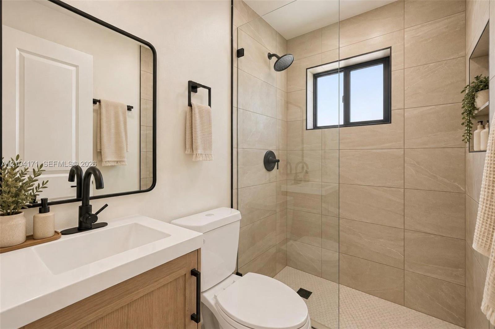 Bathroom featuring a wood-finish vanity with a white countertop, matte black hardware, a glass-enclosed shower with large-format tile surround, and a built-in shower niche