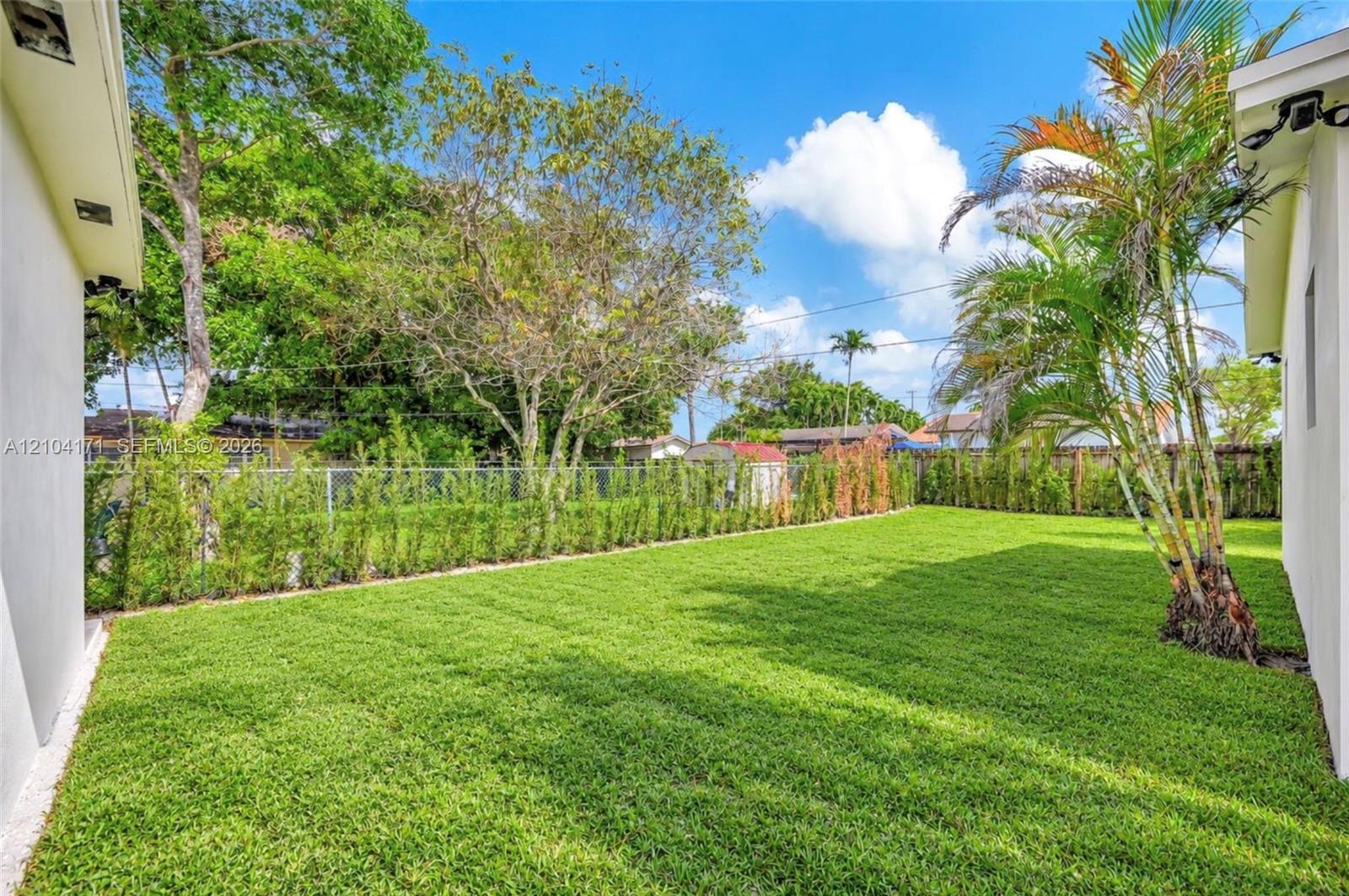 Backyard featuring a manicured lawn, perimeter fencing, and established landscape greenery