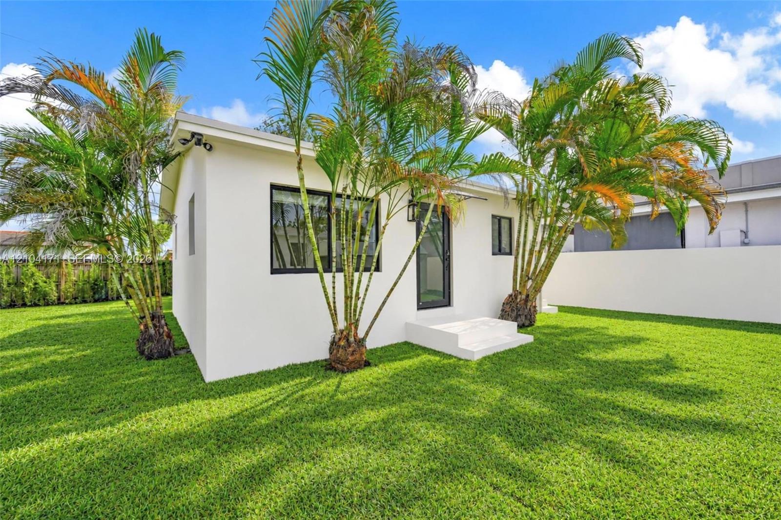 Exterior of white stucco structure featuring dark-framed windows, a glass-panel door, concrete stairs, and perimeter privacy wall