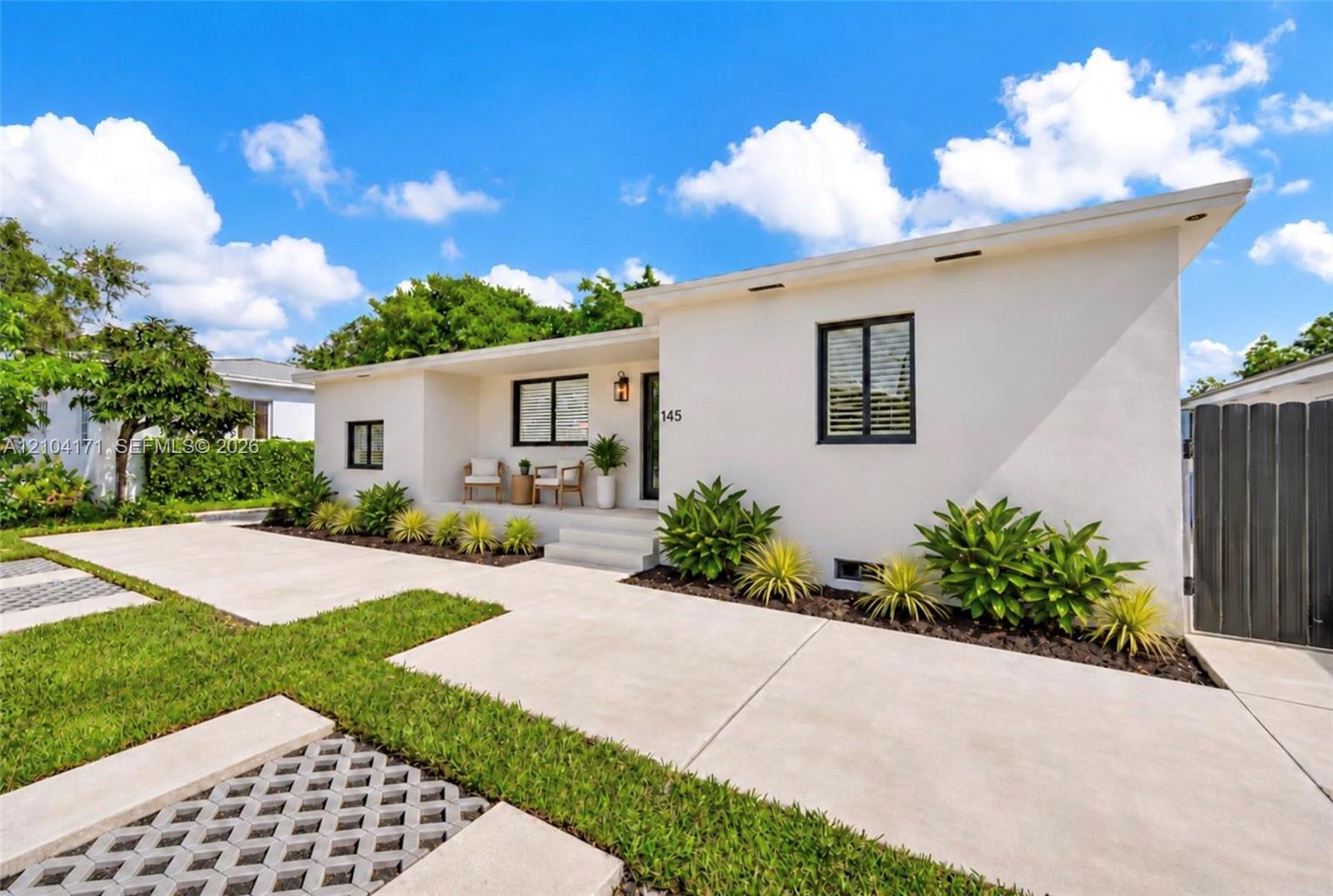 Single-story residence featuring a smooth stucco exterior, a concrete driveway, integrated recessed exterior lighting, black-framed windows, and a landscaped front garden with paver-accented lawn