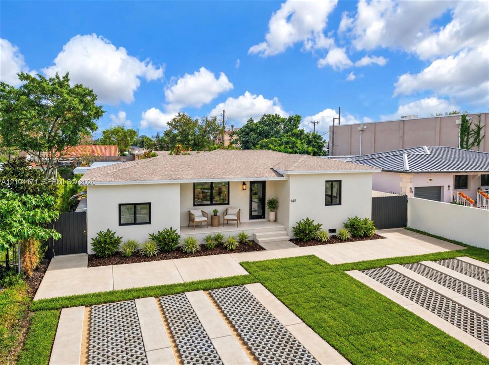 Single-story residence featuring a crisp exterior finish, a covered entryway, a roof with shingle-style materials, dark-framed windows, and a multi-section concrete driveway with integrated turf grid pavers