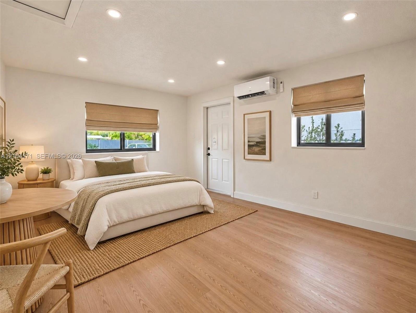 Wood-finish flooring, recessed lighting, dual windows with Roman shades, and a wall-mounted ductless mini-split system