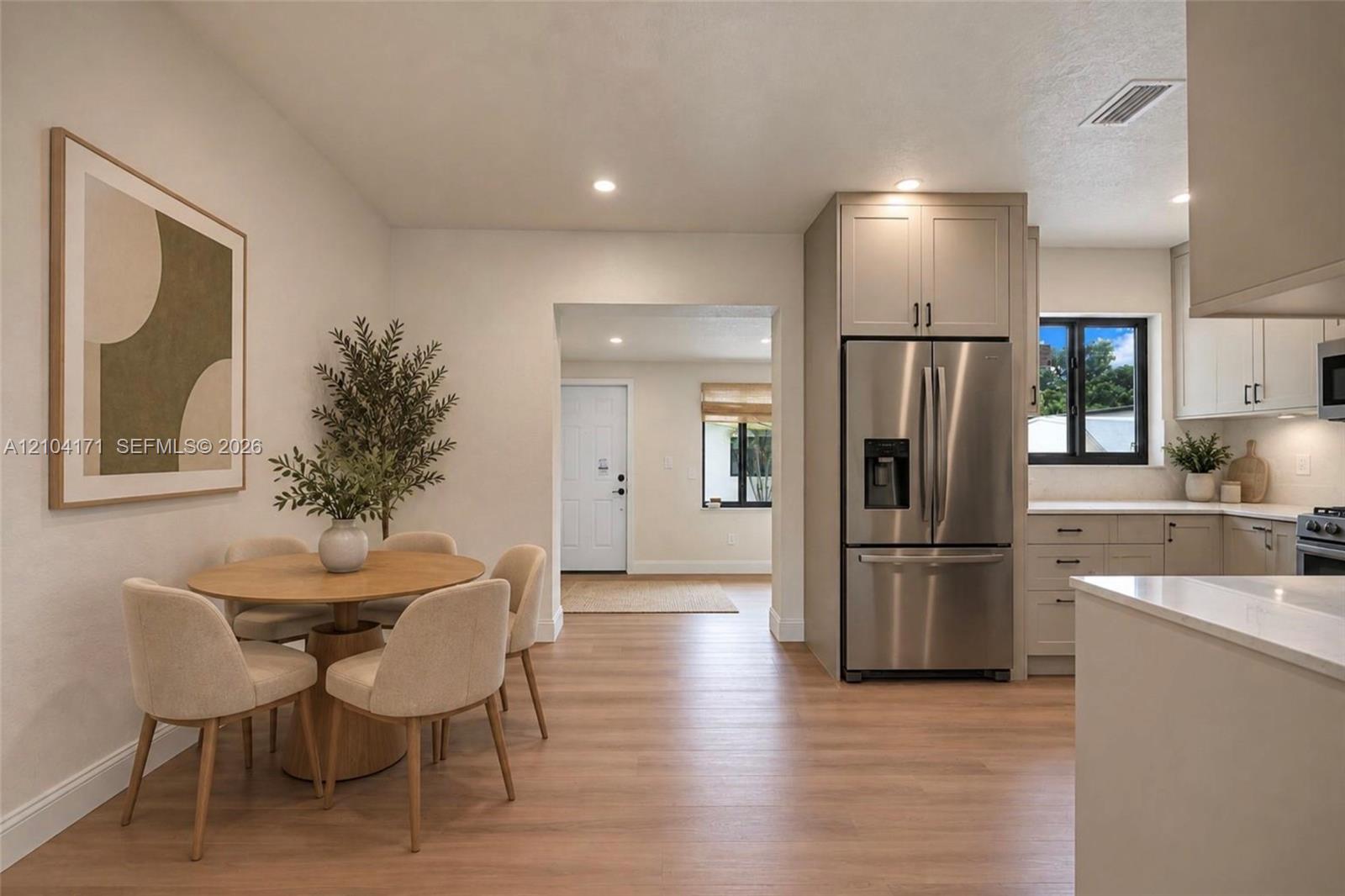 Kitchen featuring light-toned cabinetry, stainless steel refrigerator, stone countertops, and wood-finish flooring