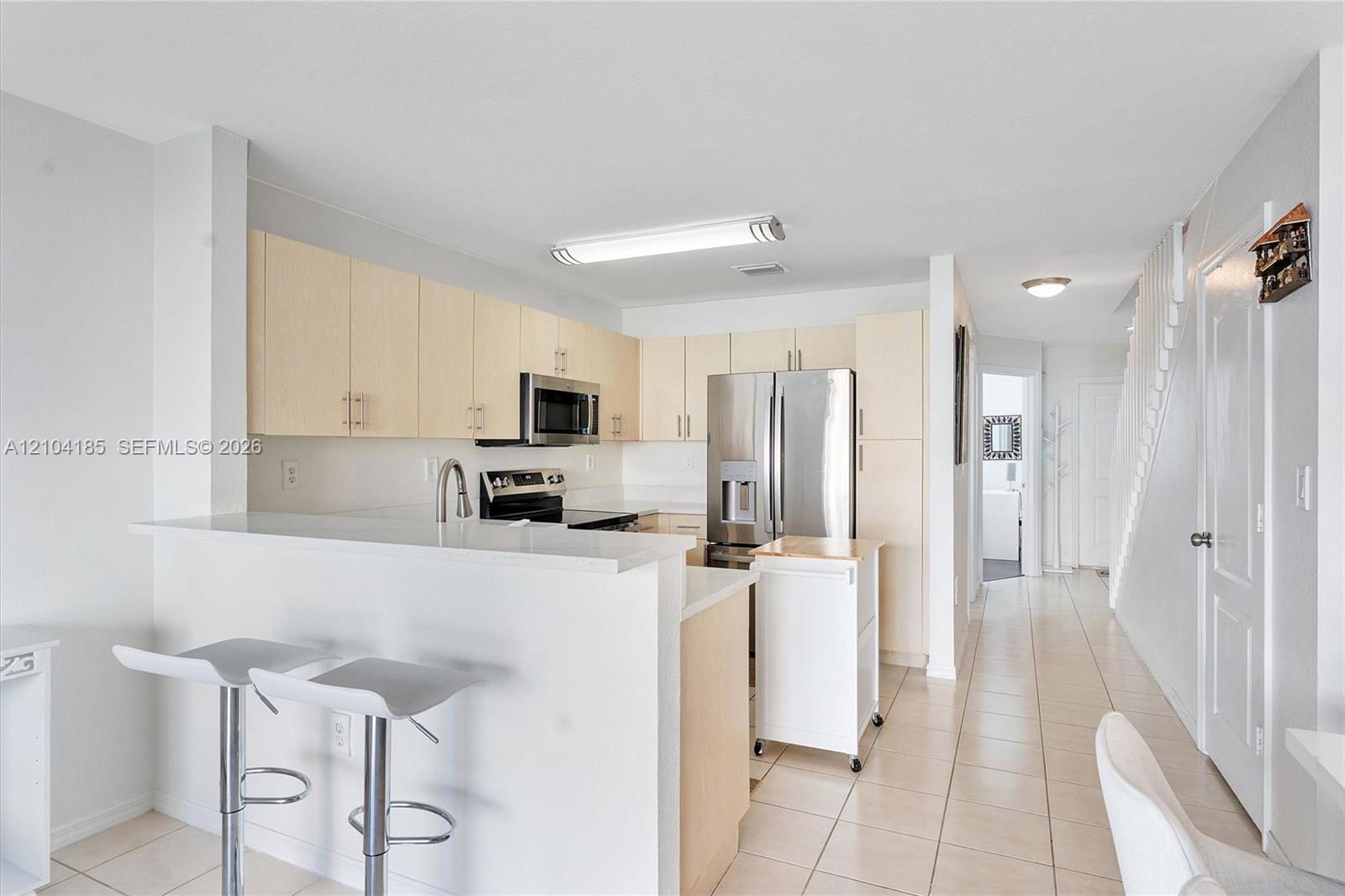 Kitchen featuring light-finish cabinetry, stainless steel appliances, a breakfast bar, and tile flooring