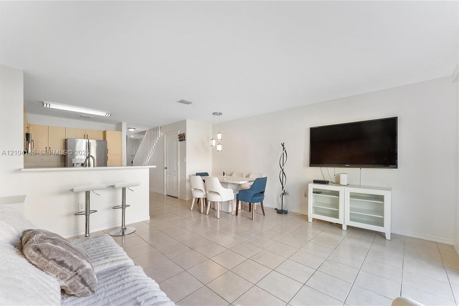 Open-concept interior featuring large-format tile flooring, light wood-finish cabinetry, a peninsula with bar seating, and recessed and pendant lighting