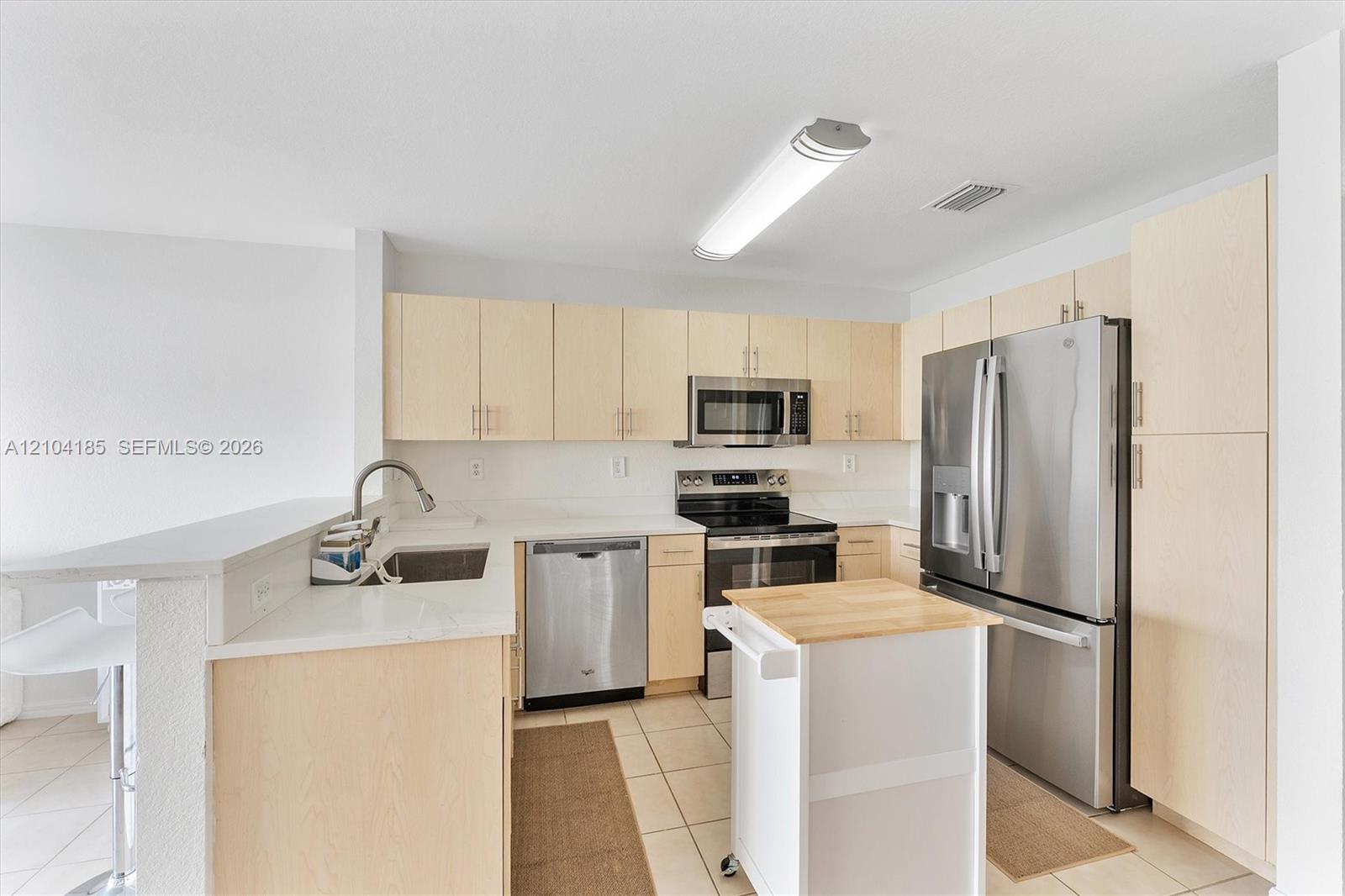 Kitchen featuring light-finish cabinetry, solid-surface countertops, stainless steel appliances, and tile flooring