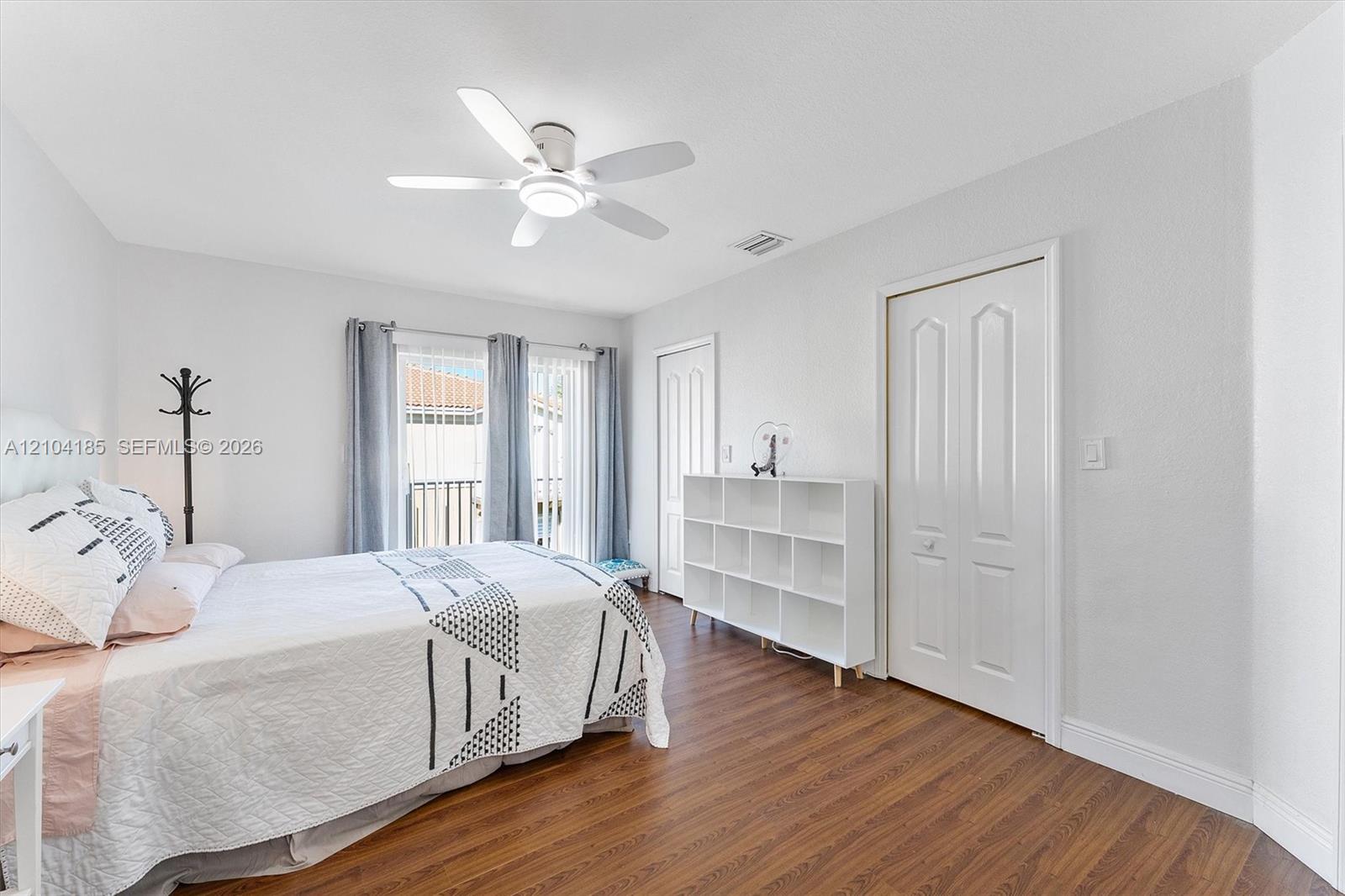 Room featuring wood-finish flooring, a multi-blade ceiling fan with integrated lighting, and dual-panel closet doors