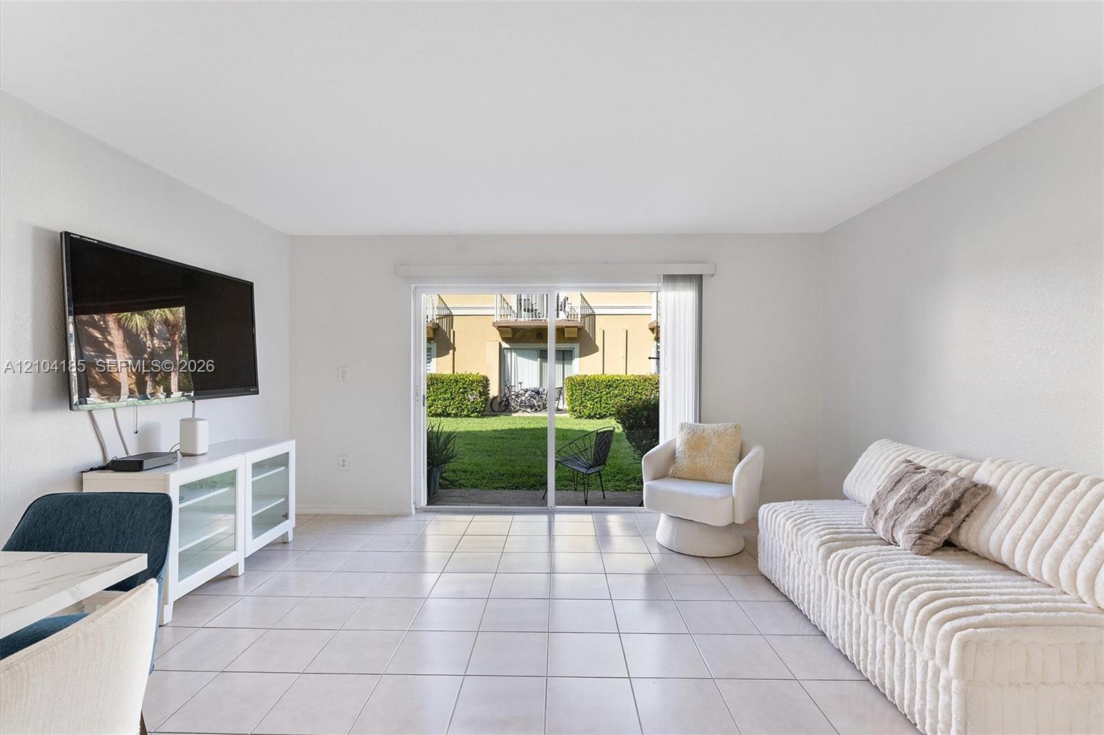 Living area featuring tile flooring and sliding glass doors opening to a concrete patio and manicured lawn