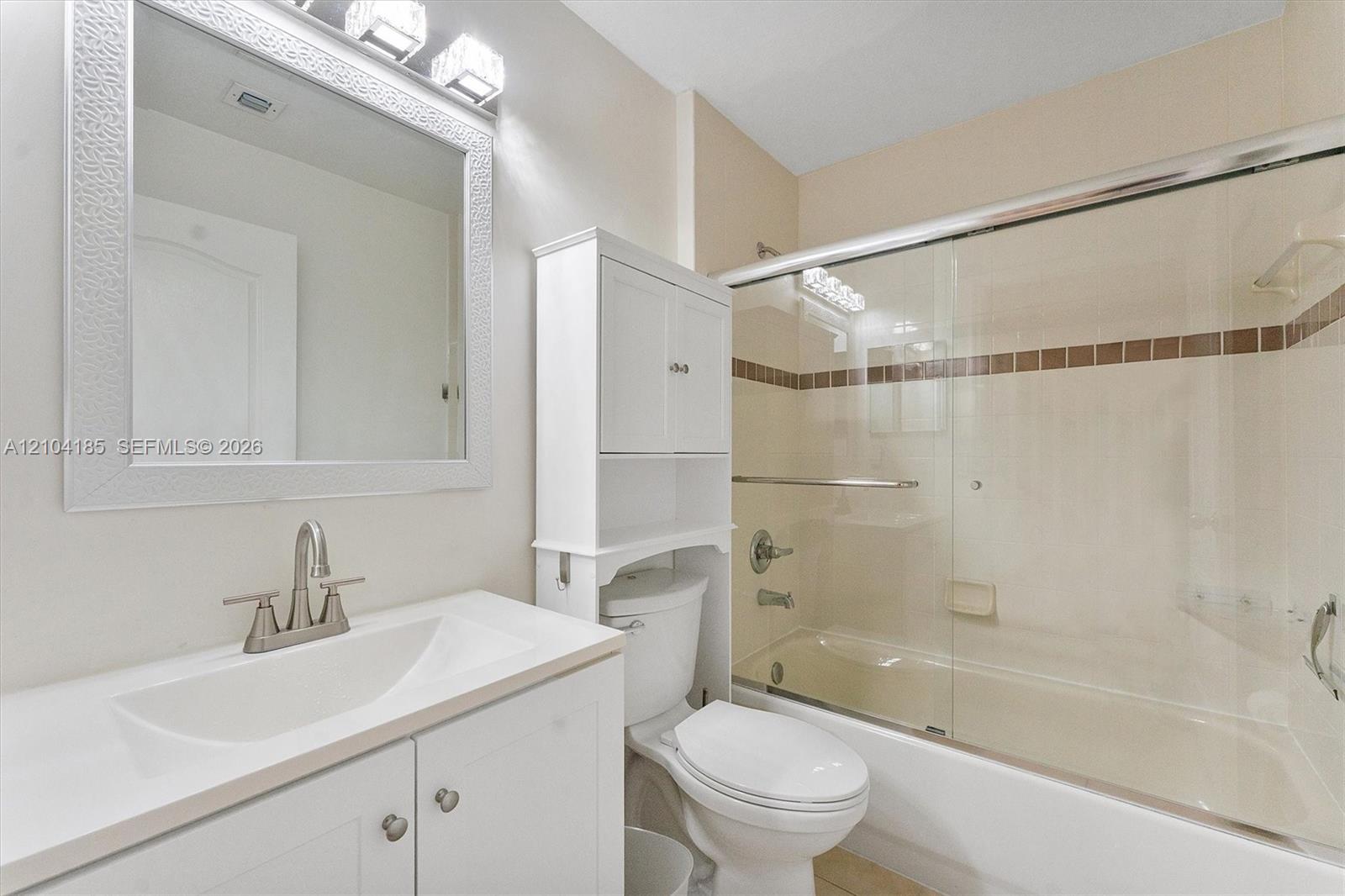 Bathroom featuring a vanity with an integrated sink, built-in over-the-toilet storage cabinet, framed wall mirror, and a tub-shower combination with sliding glass doors