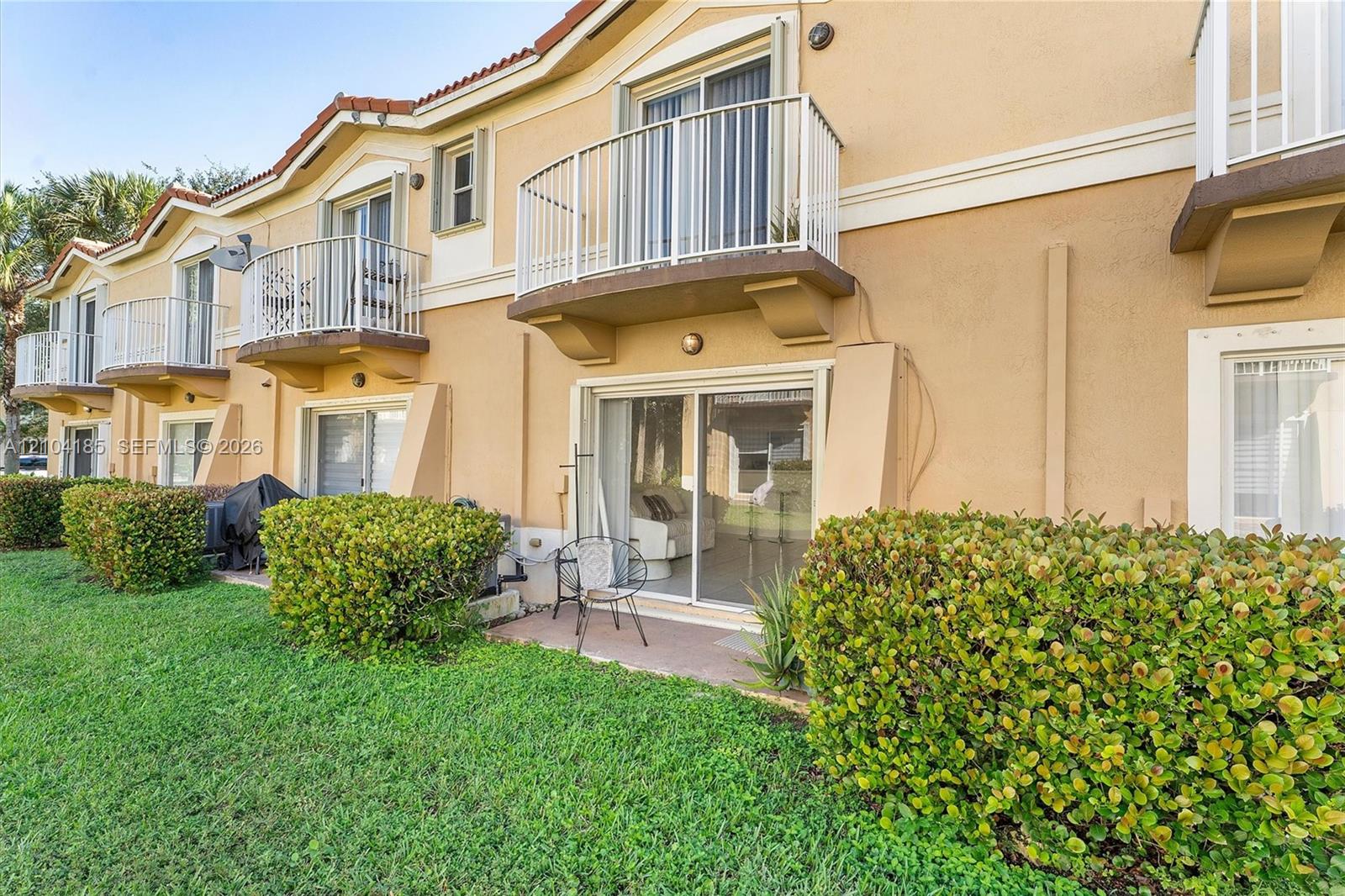 Stucco exterior featuring multiple private balconies with white metal railings, sliding glass doors, and a ground-level patio area