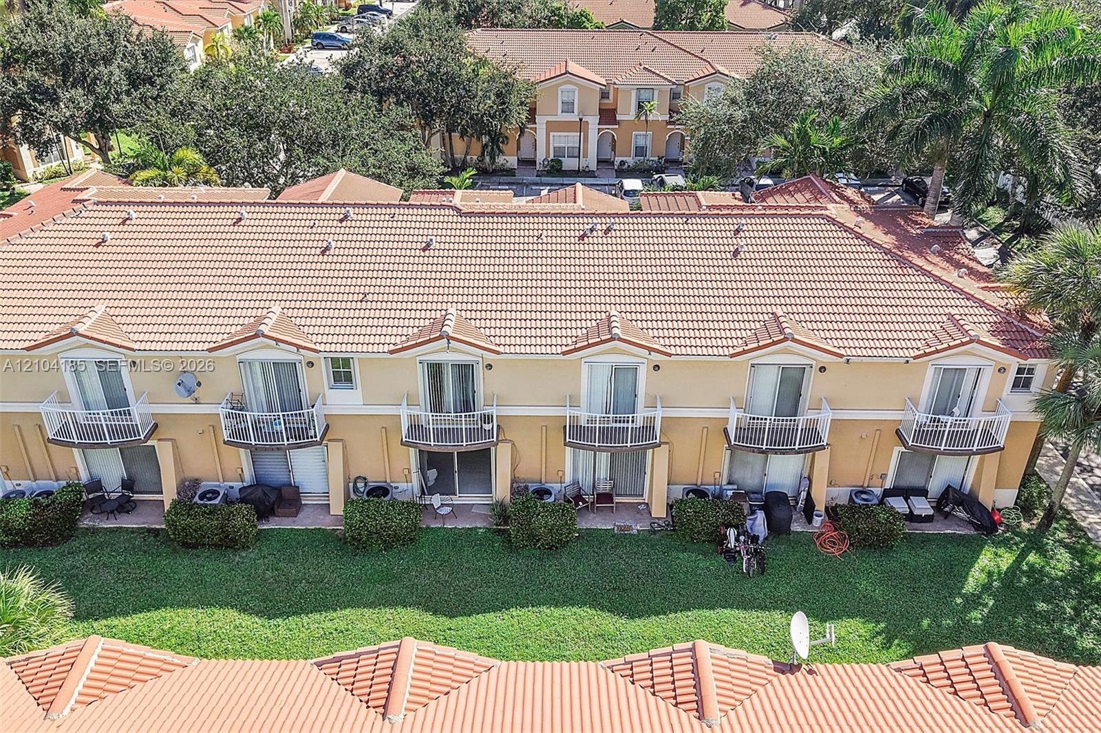Multi-unit building exterior featuring a tile roof, stucco facade, and individual upper-level balconies with white metal railings