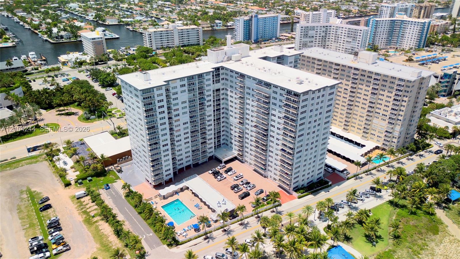 High-rise residential building featuring multiple private balconies, a ground-level swimming pool, on-site parking, and immediate proximity to coastal waterways