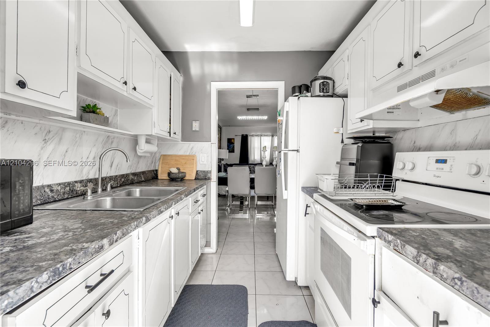 Kitchen featuring white cabinetry, stone-patterned laminate countertops, marble-patterned backsplash, stainless steel dual-basin sink, and ceramic tile flooring