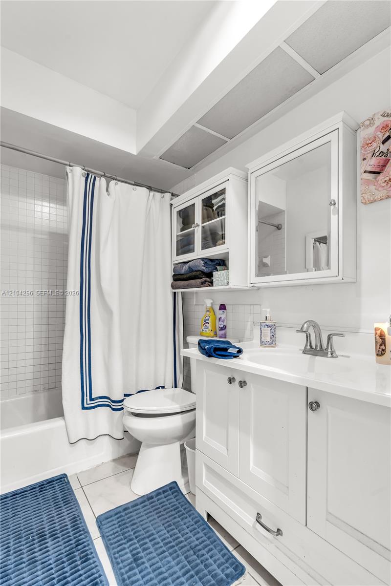 Bathroom featuring a white vanity cabinet with a integrated sink, brushed-finish faucet, wall-mounted medicine cabinet with glass-front storage, and a tiled shower surround