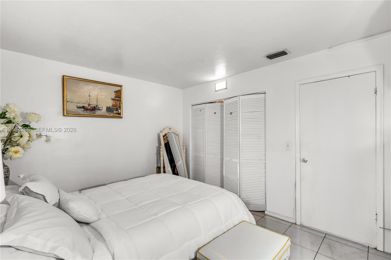 Neutral-toned interior space featuring light-colored tile flooring, white walls, and triple-panel louvered closet doors
