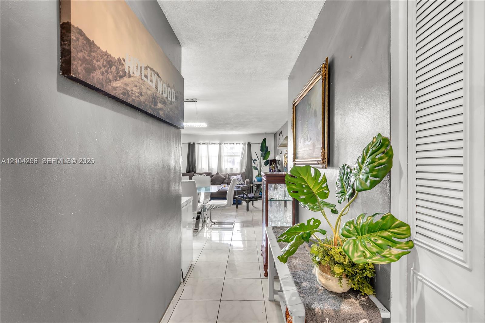 Interior hallway featuring light-colored tile flooring, smooth neutral-tone walls, and a white louvered closet door