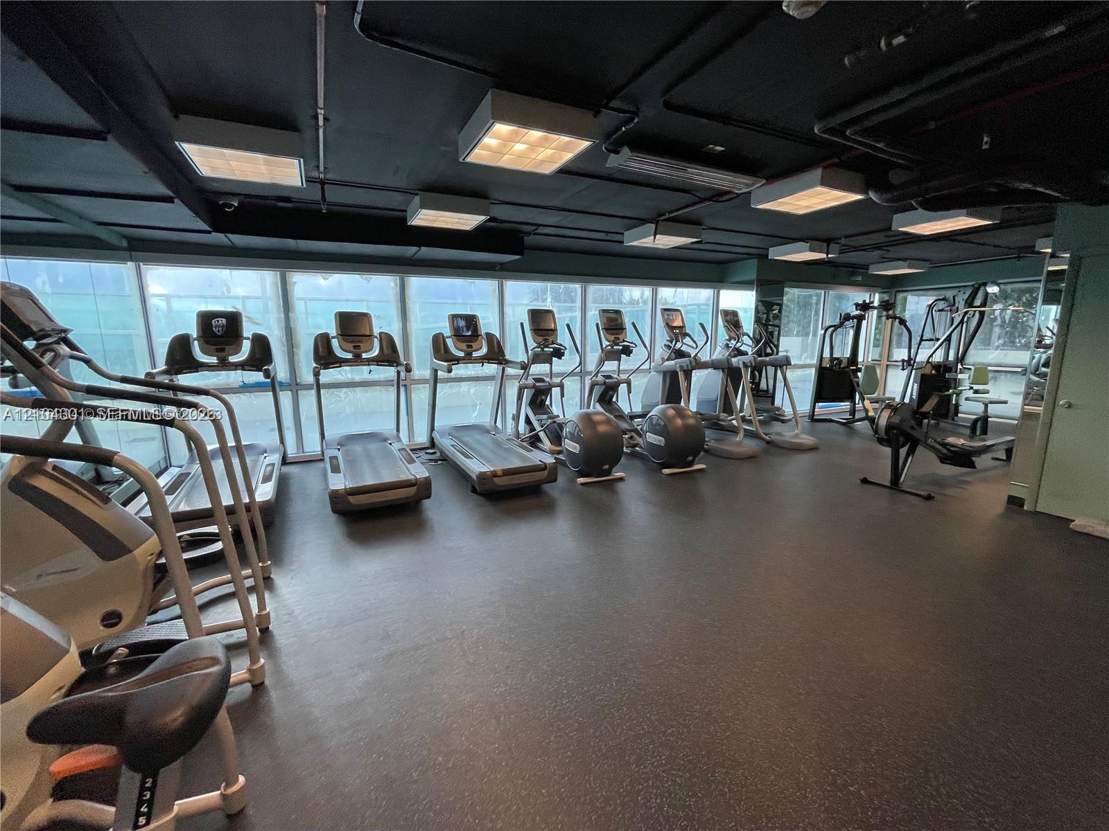 Fitness center featuring expansive floor-to-ceiling windows, industrial-style exposed ceiling, and specialized rubberized flooring