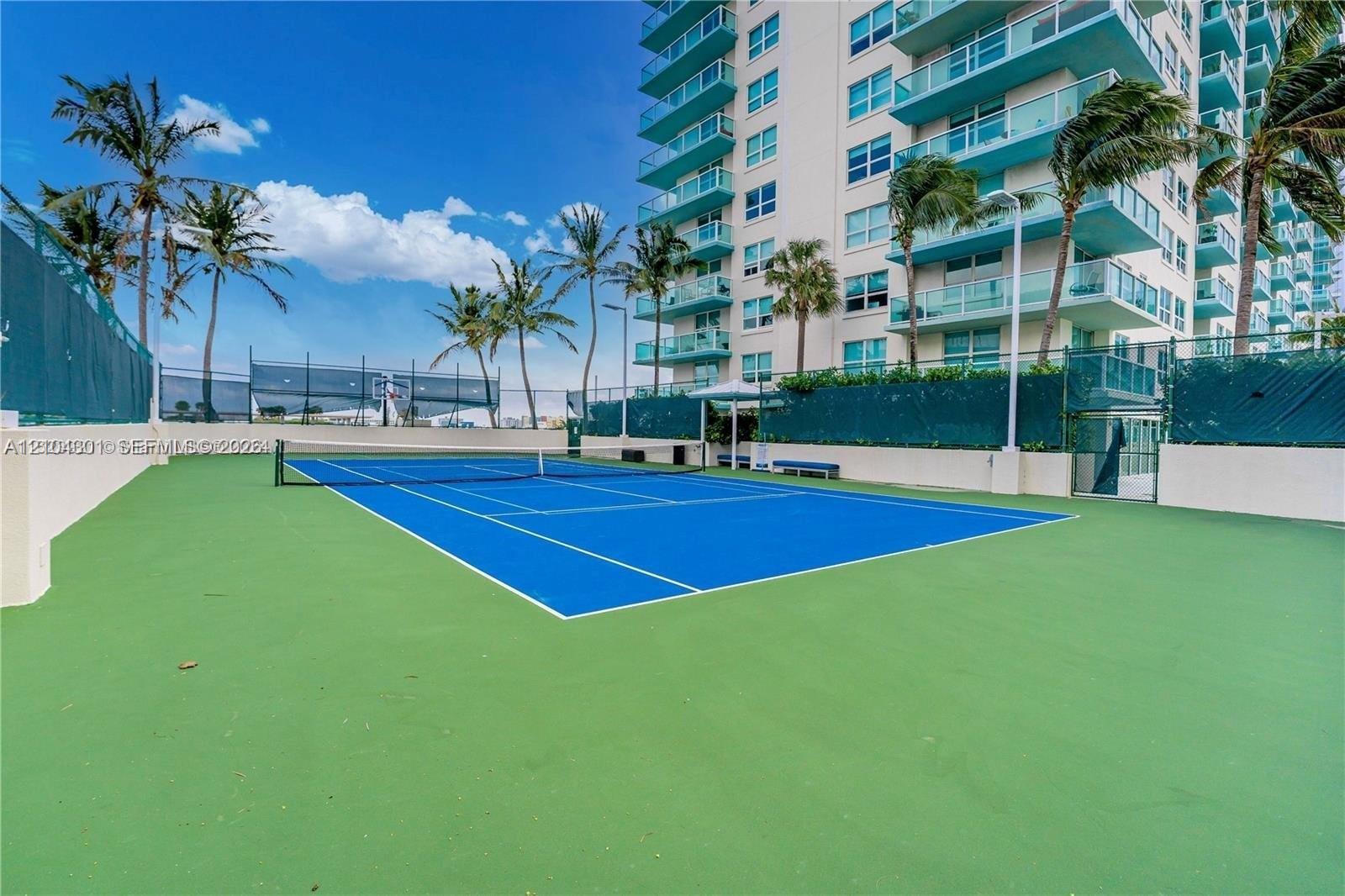 Tennis court with blue surface, perimeter fencing, and surrounding palm trees