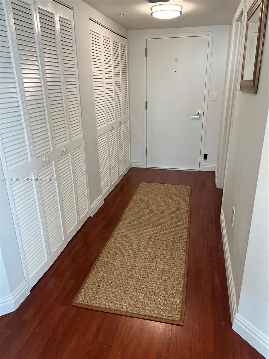 Entryway featuring wood-finish flooring, dual white louvered-door closets, and a flush-mount ceiling light fixture