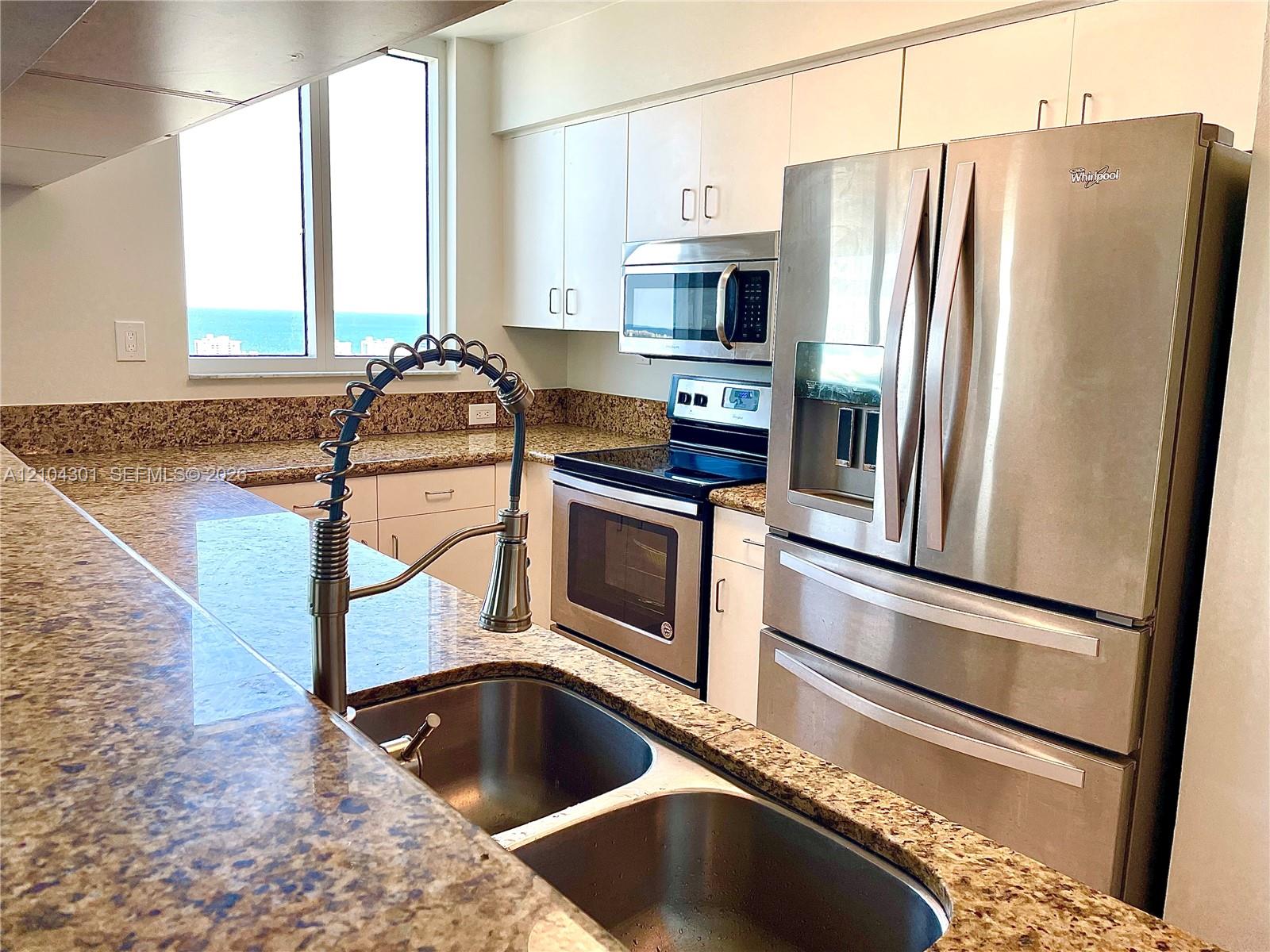 Kitchen featuring stone countertops, stainless steel appliances, white cabinetry, a dual-basin sink with a gooseneck faucet, and natural light