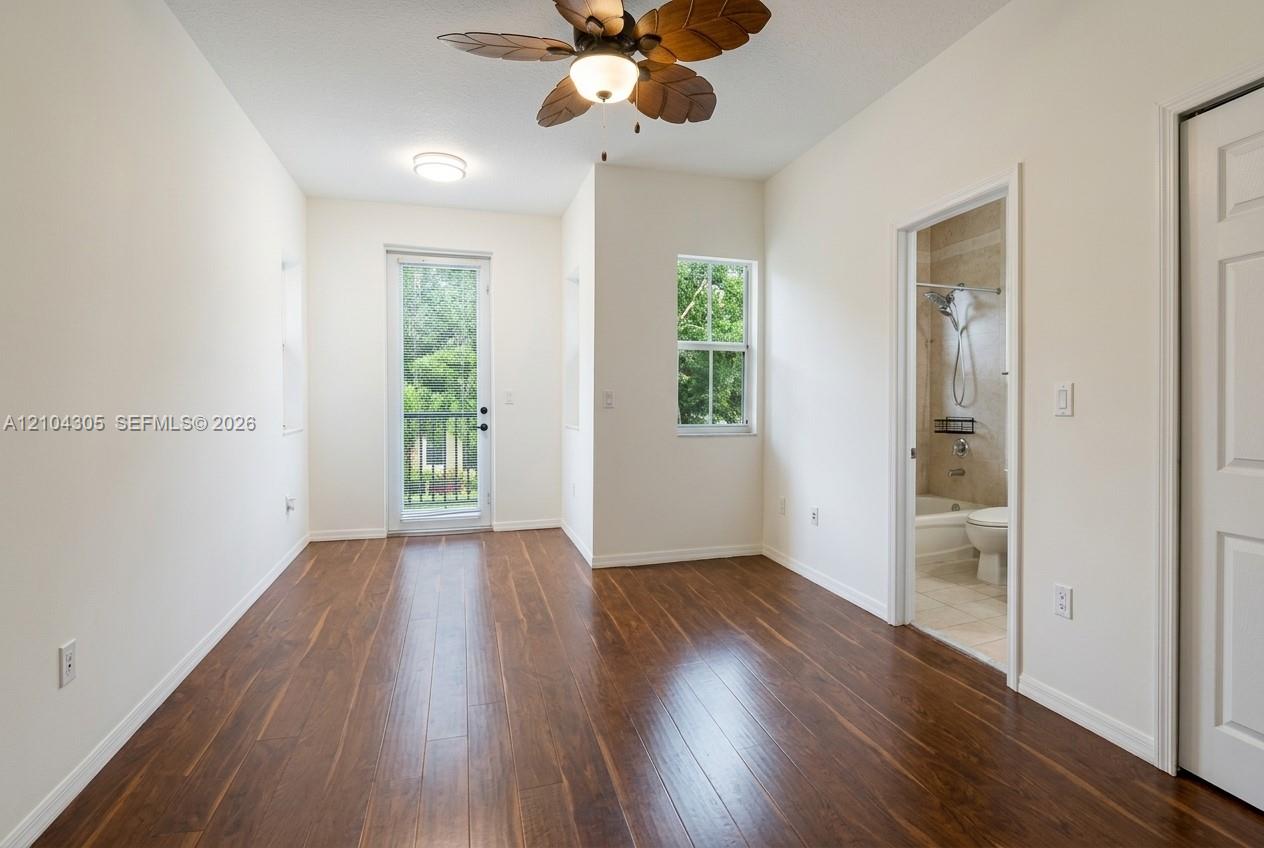 Room featuring wood-finish flooring, ceiling fan with palm-style blades, single-pane windows, glass-panel entry door, and multi-panel interior door