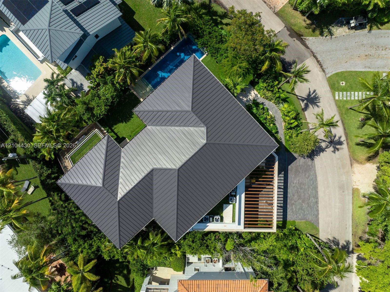 Aerial perspective featuring a metal roof, rectangular swimming pool, integrated patio pergola, and mature landscaping