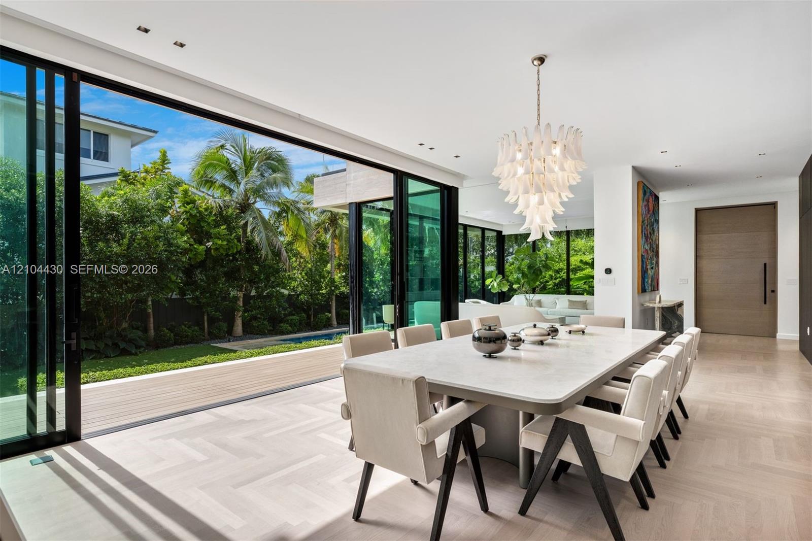 Floor-to-ceiling sliding glass walls, light-toned chevron-patterned wood-finish flooring, sculptural multi-tier chandelier, and recessed ceiling lighting