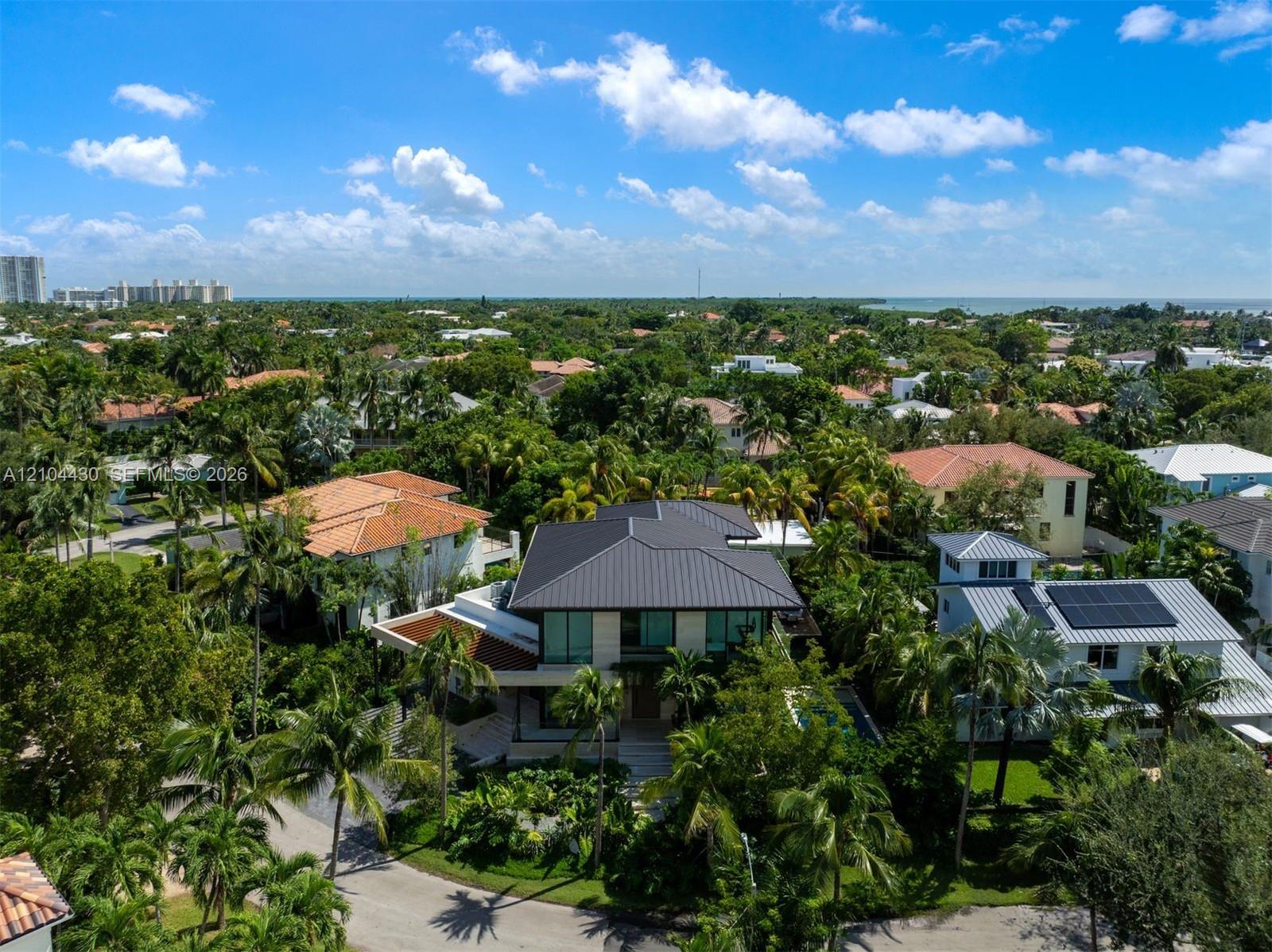 Aerial perspective of a multi-story residence featuring a dark metal roof, expansive glass windows, and mature tropical landscaping within a coastal environment