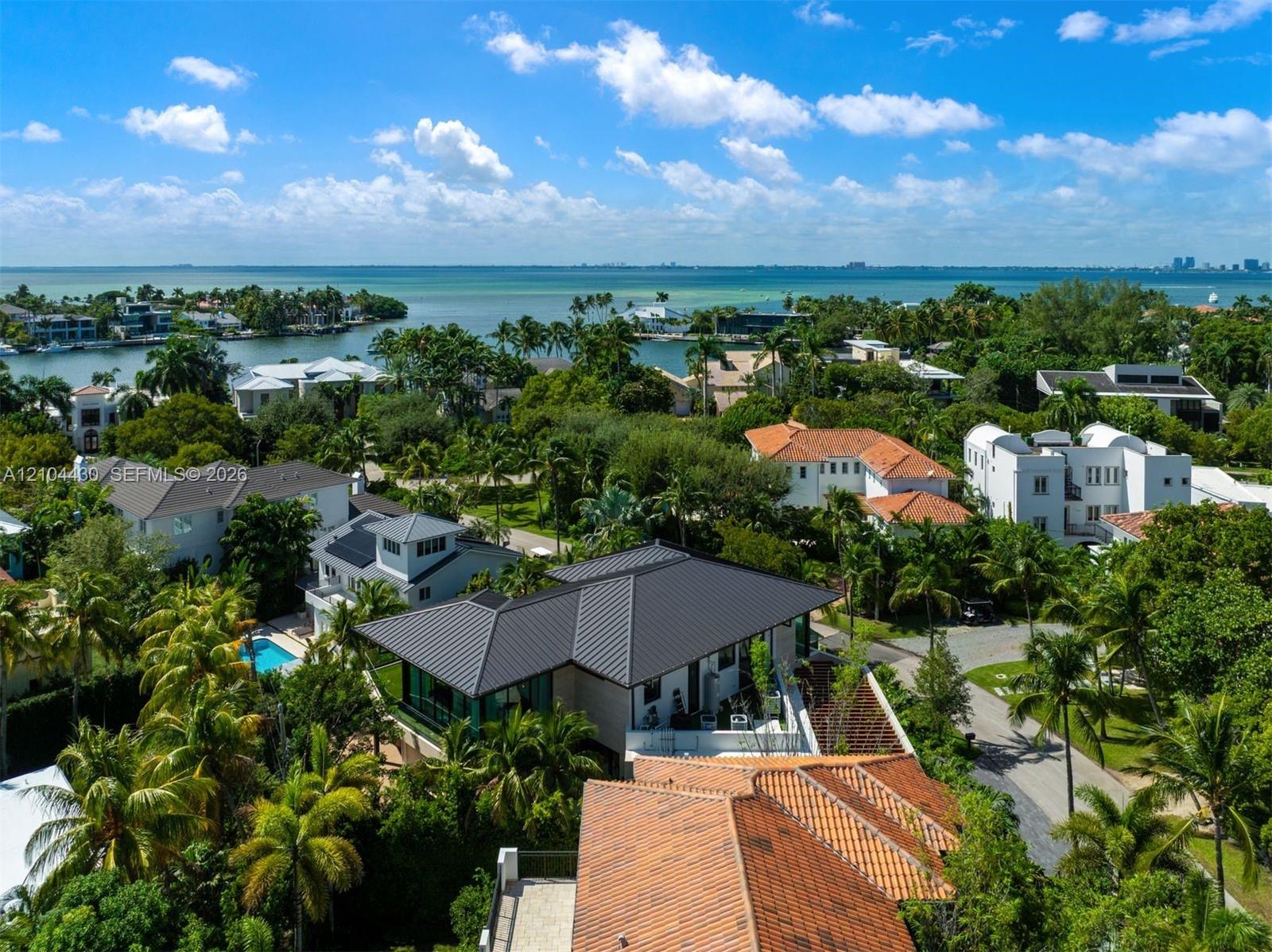 Aerial perspective featuring a metal roof structure, terracotta tile roofing, mature landscaping, and proximity to the coastline