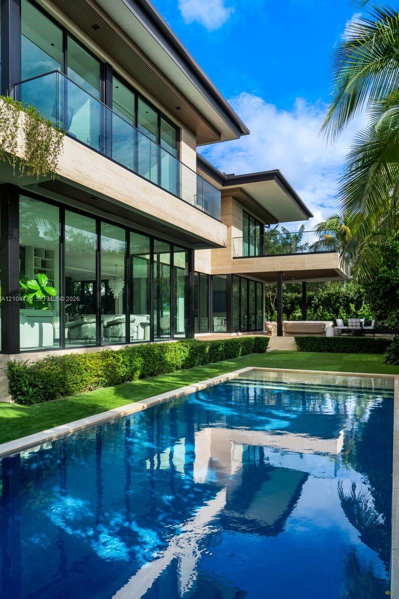 Contemporary multi-level exterior featuring floor-to-ceiling glass walls, sleek glass balcony railings, stone-finish cladding, and a private swimming pool with integrated hardscaping