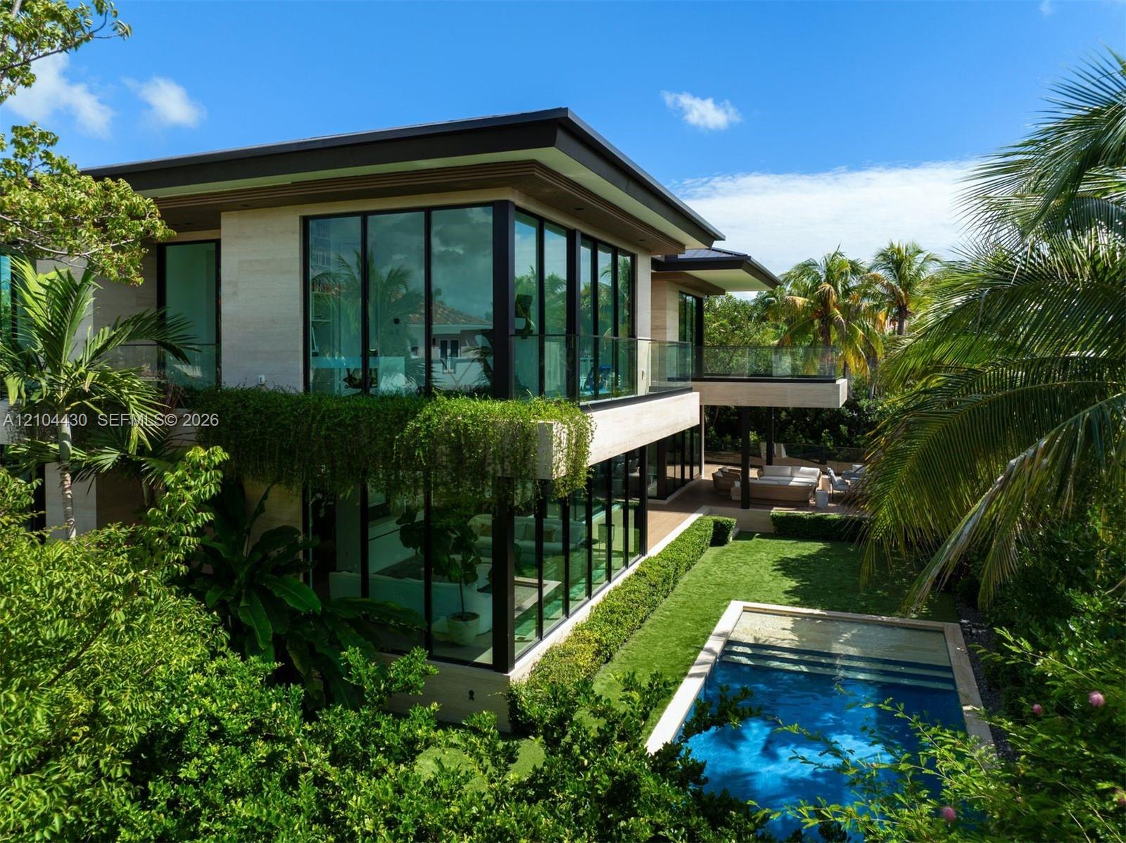 Modern architectural residence featuring floor-to-ceiling windows, stone exterior cladding, a second-story glass-railed balcony, an in-ground swimming pool, and manicured landscaping