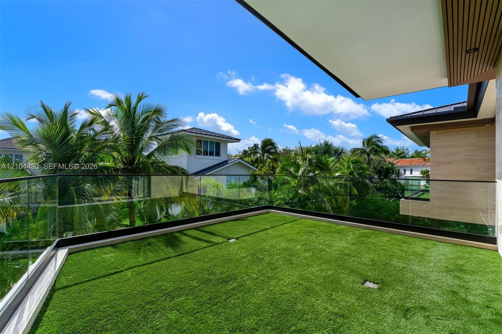 Elevated outdoor terrace featuring synthetic turf flooring, frameless glass railings, and a covered ceiling with slatted wood-finish detailing