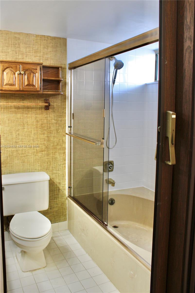 Bathroom featuring a tub-shower combination with glass sliding doors, white tile surround, built-in wooden cabinetry, and textured wall finish