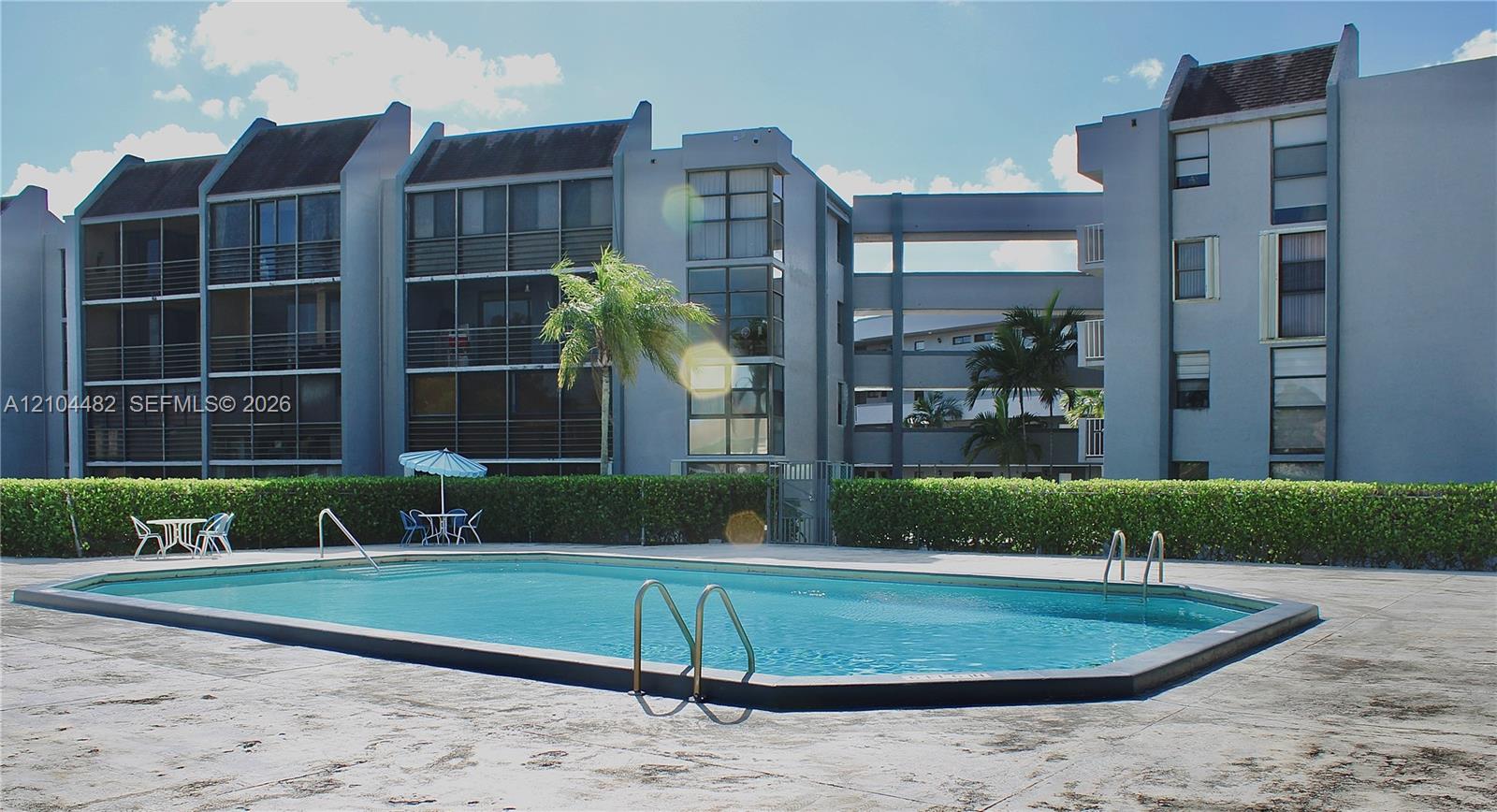 Rectangular swimming pool featuring a concrete deck, metal handrails, and a surrounding privacy hedge