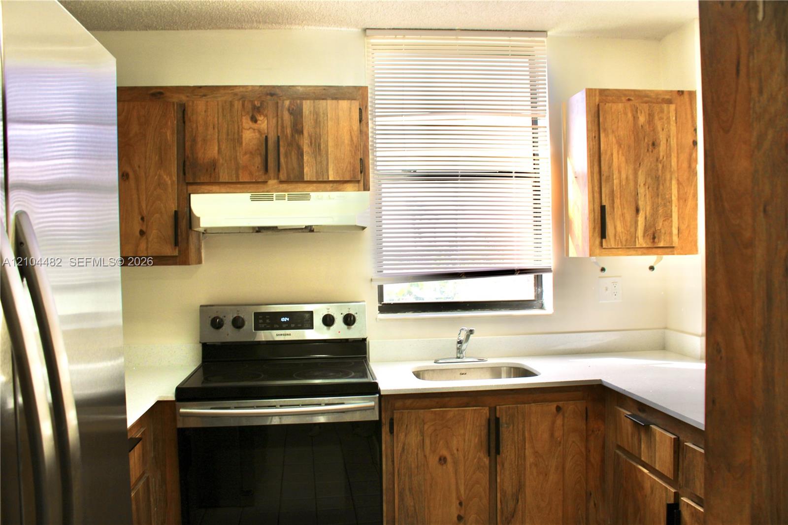 stainless steel appliances, solid surface countertops, a stainless steel sink, and a window with horizontal blinds