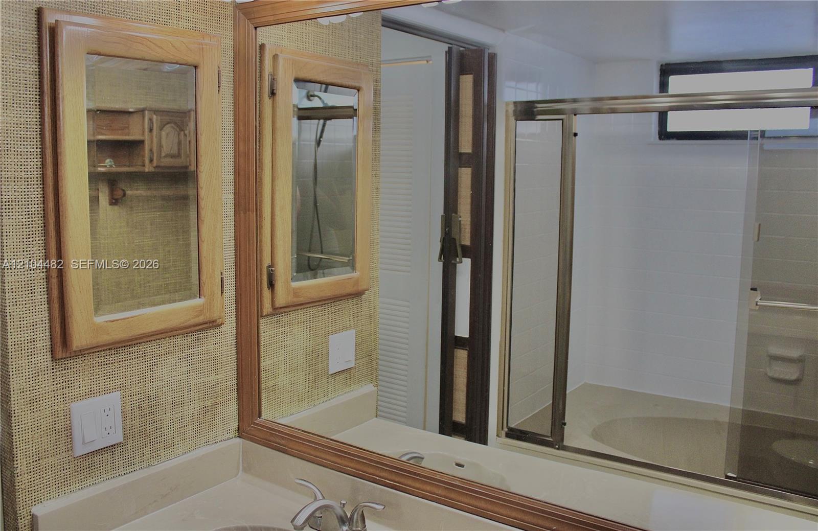 Bathroom featuring dual wood-framed medicine cabinets, a large wall-mounted mirror, a neutral-toned integrated sink vanity, and a sliding glass-door shower enclosure