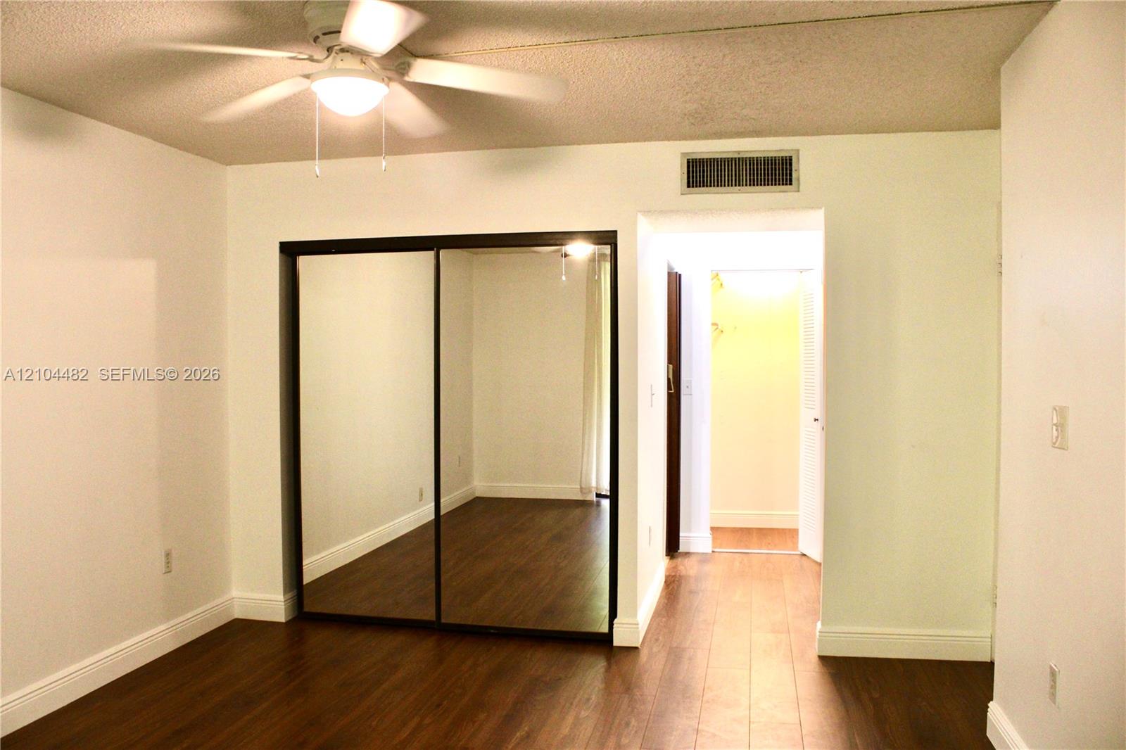 Wood-finish flooring, ceiling fan with integrated lighting, and mirrored sliding closet doors